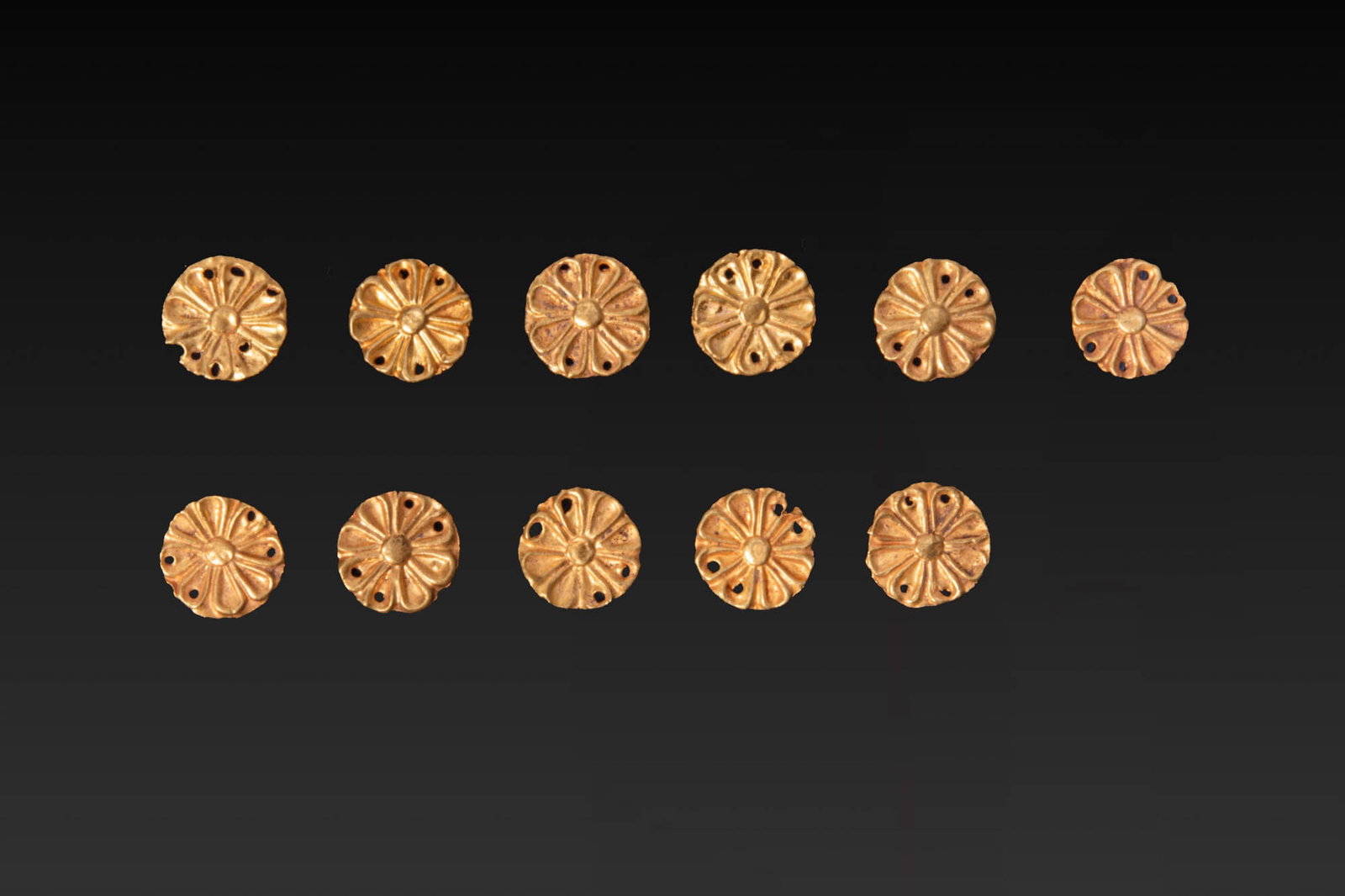 COLLECTION OF GREEK GOLD ROSETTE APPLIQUES: Ca. 600 - 200 BC. A collection of 11 gold rosette appliques, each with a raised central boss surrounded by radiating almond-shaped petals in repousse. Small perforations are pierced around the perimet