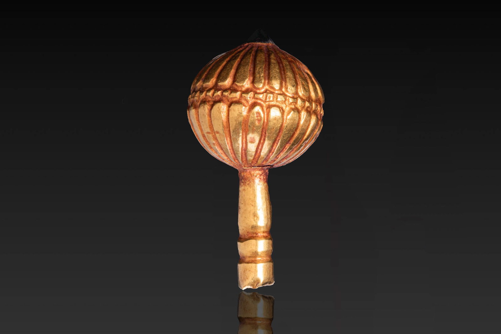 GREEK GOLD RIBBED PIN HEAD WITH GARNET: Ca. 800 - 600 BC. A gold pin head of globular shape, formed with vertical ribbing divided at the centre by a narrow collar, with a garnet at the apex. The cylindrical shaft is encircled by two moulded