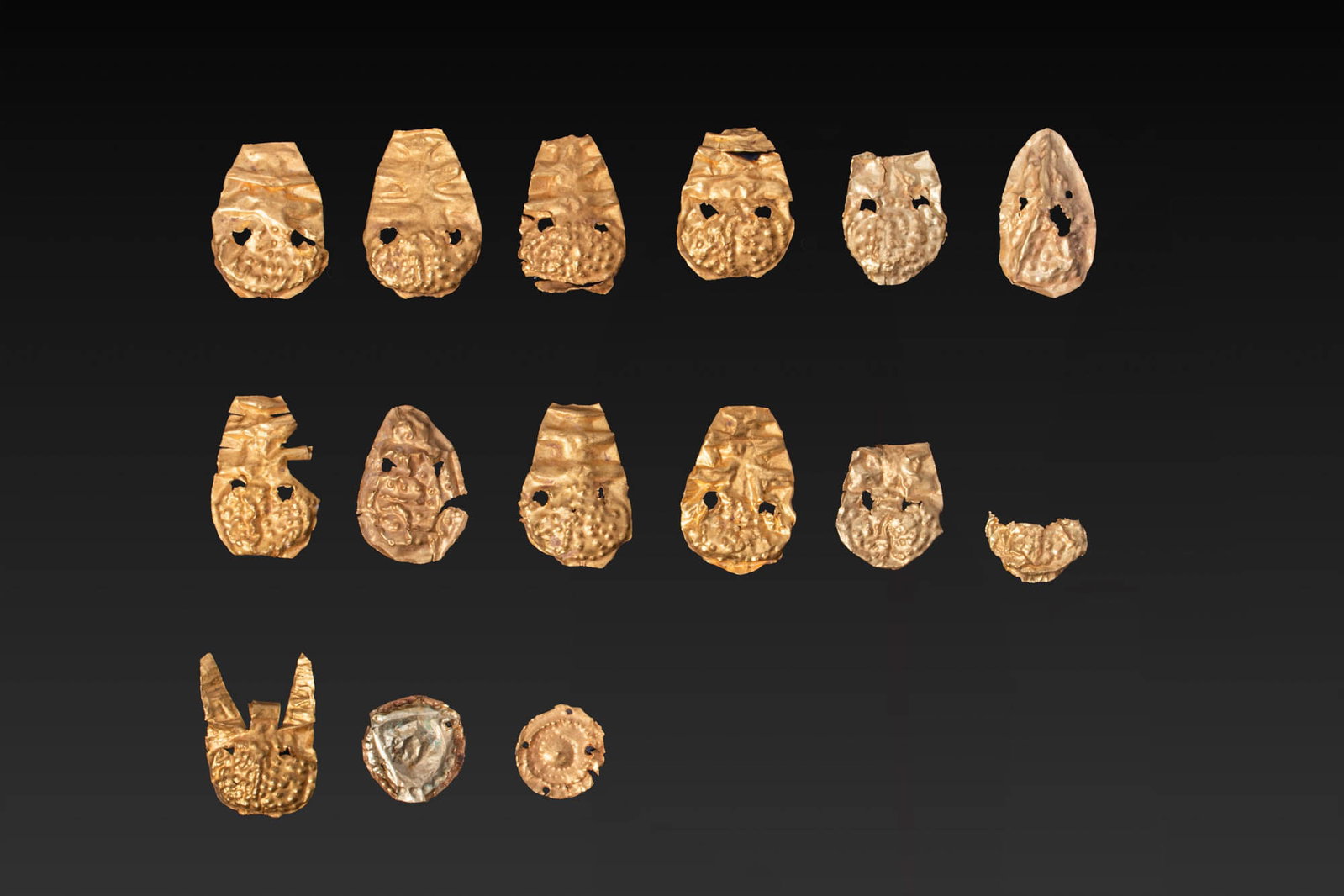 COLLECTION OF GREEK GOLD APPLIQUES: Ca. 700 - 500 BC. A collection of 15 gold appliques, including 13 thin sheet repousse drop-shaped elements, each decorated with a pellet-covered rounded end below transverse ribs in the upper tapering