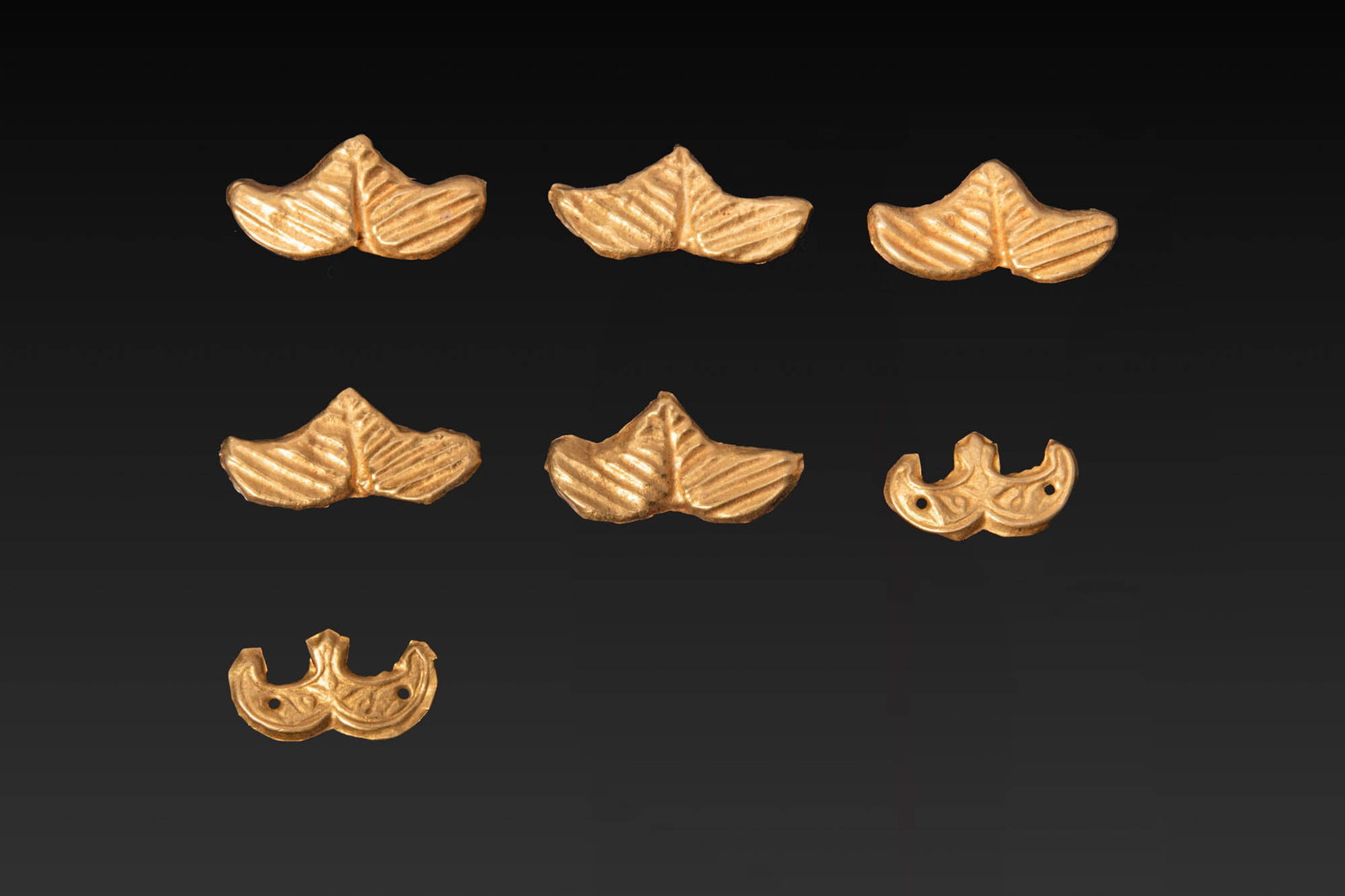 COLLECTION OF GREEK GOLD APPLIQUES: Ca. 700 - 500 BC. A collection of seven gold appliques including five of leaf-shaped form with a central ridge and diagonal veining, and two crescent-shaped pieces with a central projection and pierce
