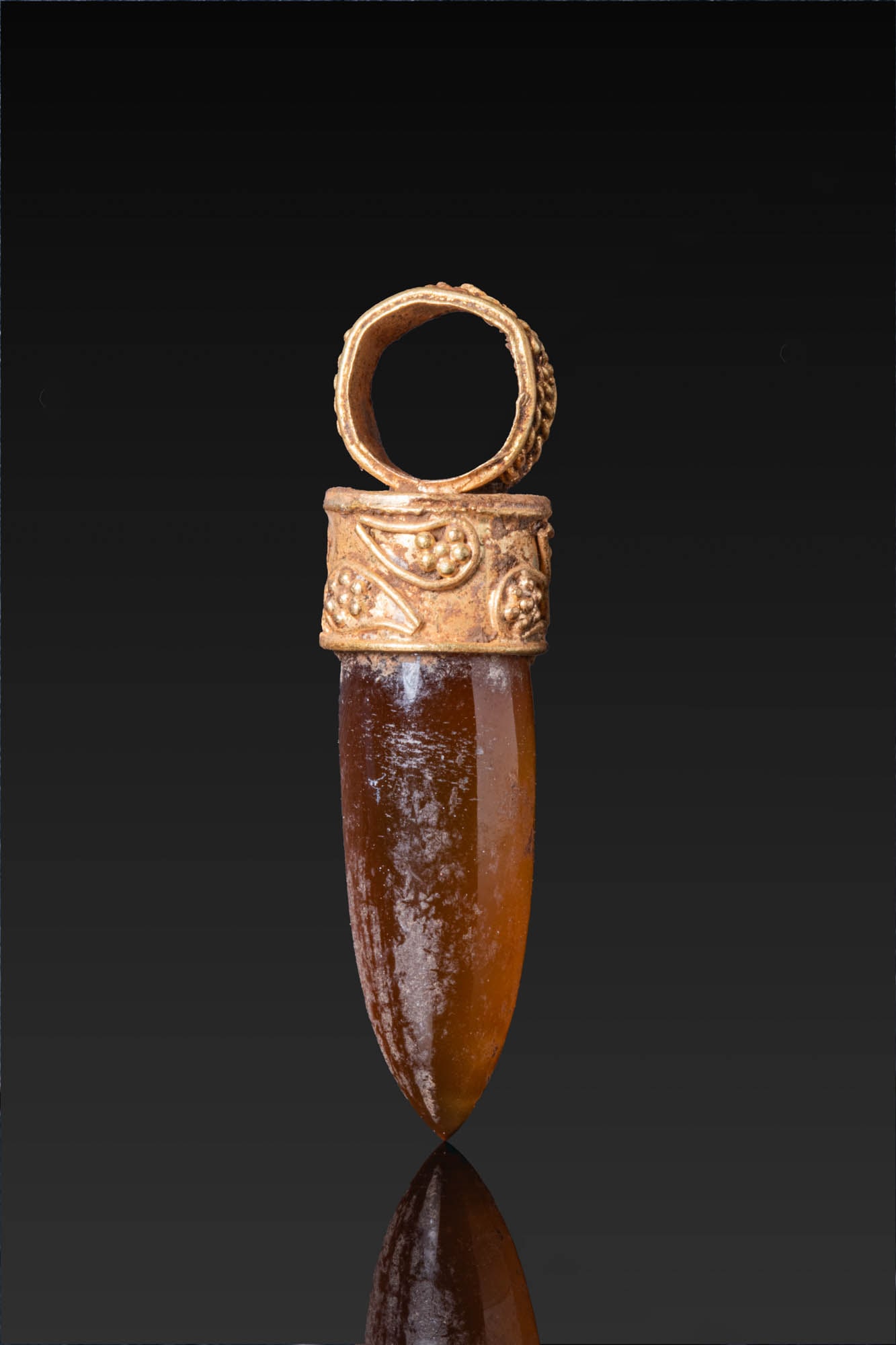 HELLENISTIC HIGH KARAT GOLD PENDANT WITH CARNELIAN: Ca. 300 - 100 BC. A gold pendant set with a tapered carnelian drop in a circular mount with a plain upper plate, the collar and suspension loop decorated with granulation and drop-shaped motifs in fin