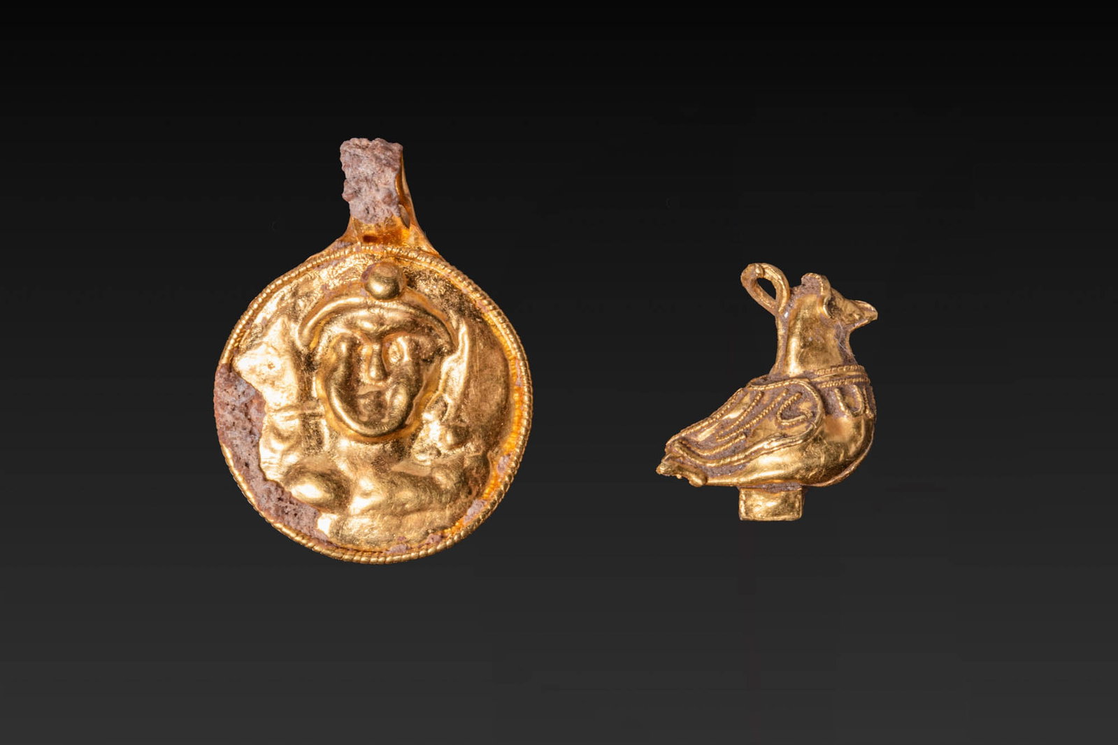 PAIR OF HELLENISTIC GOLD PENDANTS: Ca. 200 - 1 BC. A pair of gold pendants, including, from left to right: a circular pendant with a repousse bust framed by a beaded border; and a pendant in the form of a stylised bird, with applied wi
