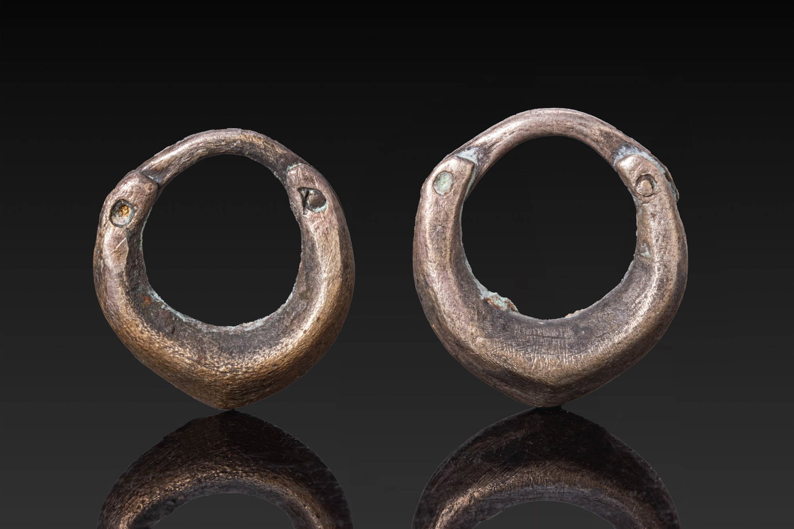 PAIR OF GREEK SILVER EARRINGS: Ca. 500 BC. A pair of silver earrings, each of circular form with a thickened lower body tapering to a narrower upper arc with a pin fastening. Size: 19-22mm x 19-20mm; Weight: 9.8g Provenance: Centra