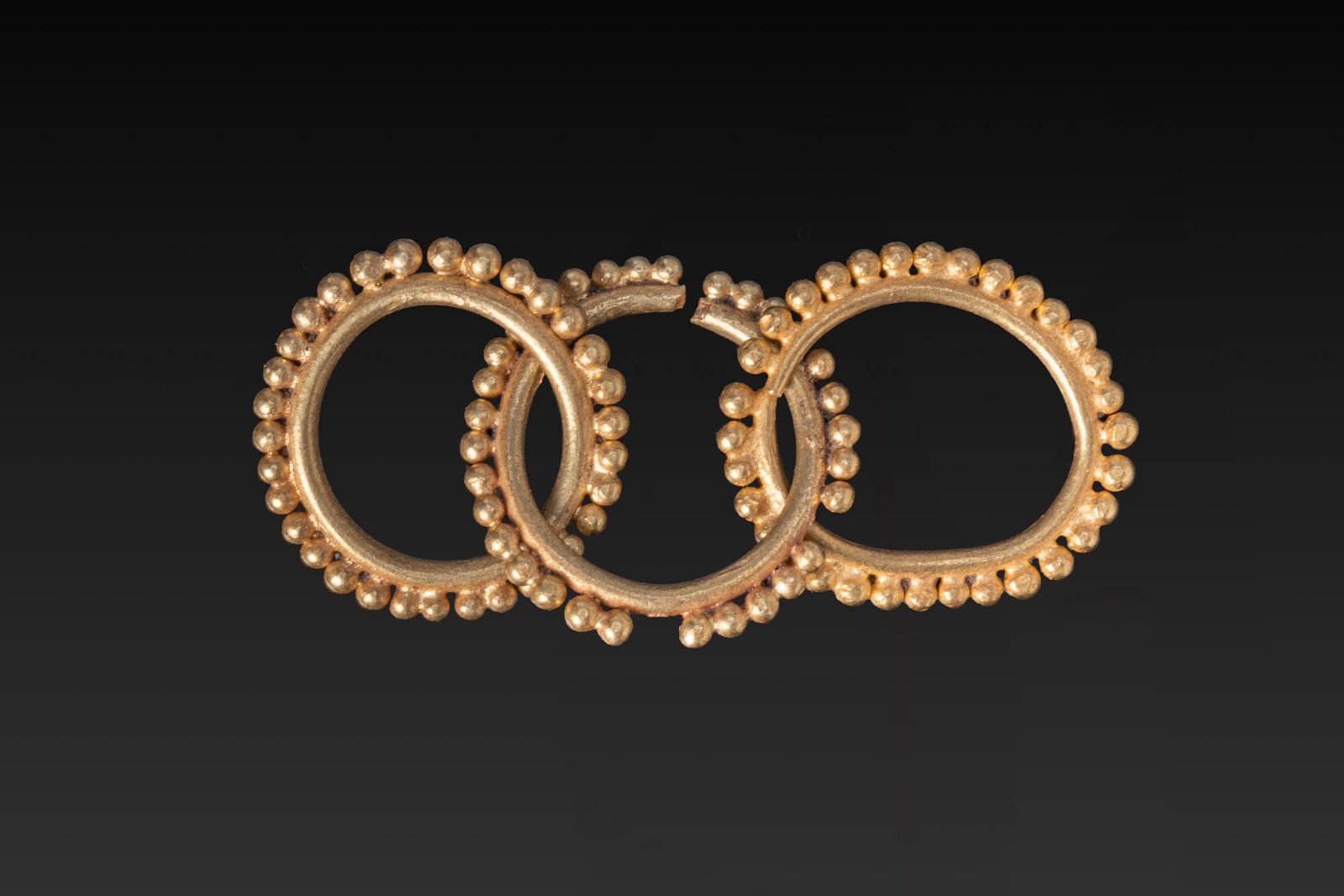 GREEK GOLD GRANULATED EARRING: Ca. 700 - 500 BC. A gold earring composed of a central penannular hoop with two hoops attached at either side, each bordered at the outer edge with a row of applied granules. Size: 29mm x 13mm; Weight