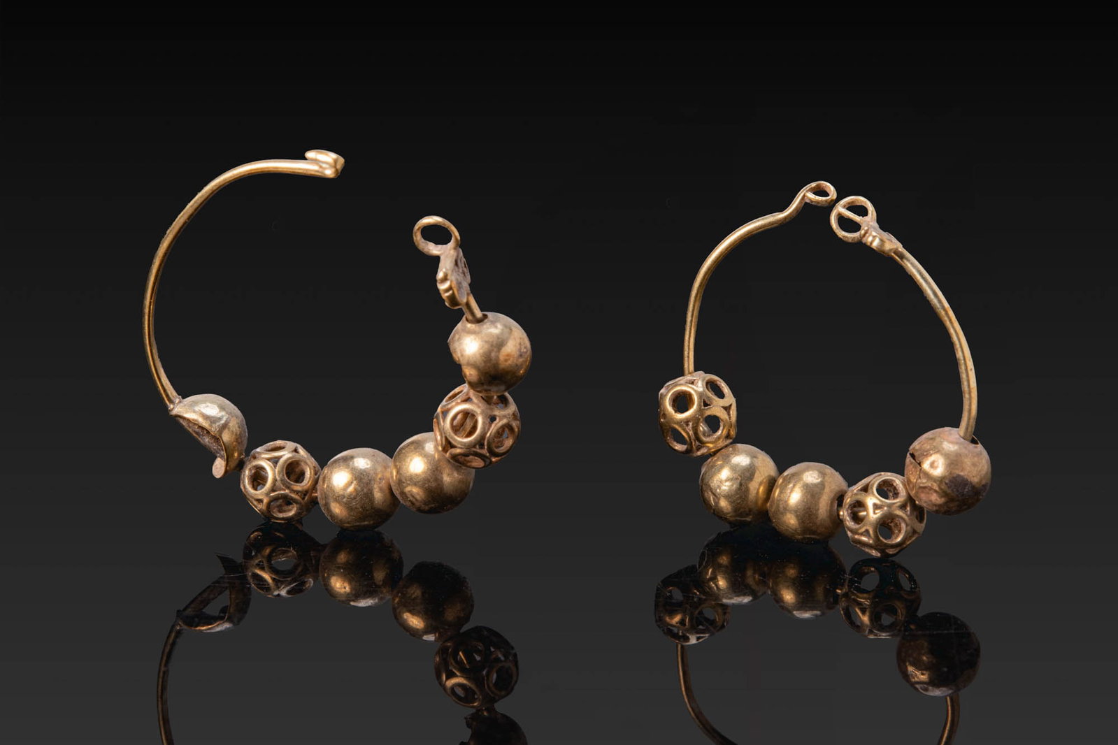 MATCHED PAIR OF HELLENISTIC GOLD EARRINGS: Ca. 300 - 100 BC. A matched pair of gold hoop earrings, each with a hook and eye closure and threaded with globular and openwork spherical beads. Size: 21-23mm x 20-22mm; Weight: 2.1g Provenance: From