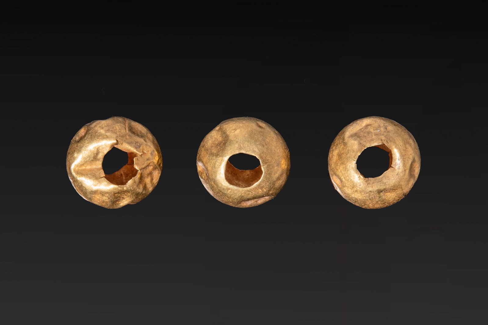 COLLECTION OF GREEK GOLD BEADS: Ca. 500 BC. A collection of three gold beads, each of rounded form with a large central perforation. Size: 10-10mm x 5-6mm; Weight: 1g Provenance: From a private UK collection; London art market purch
