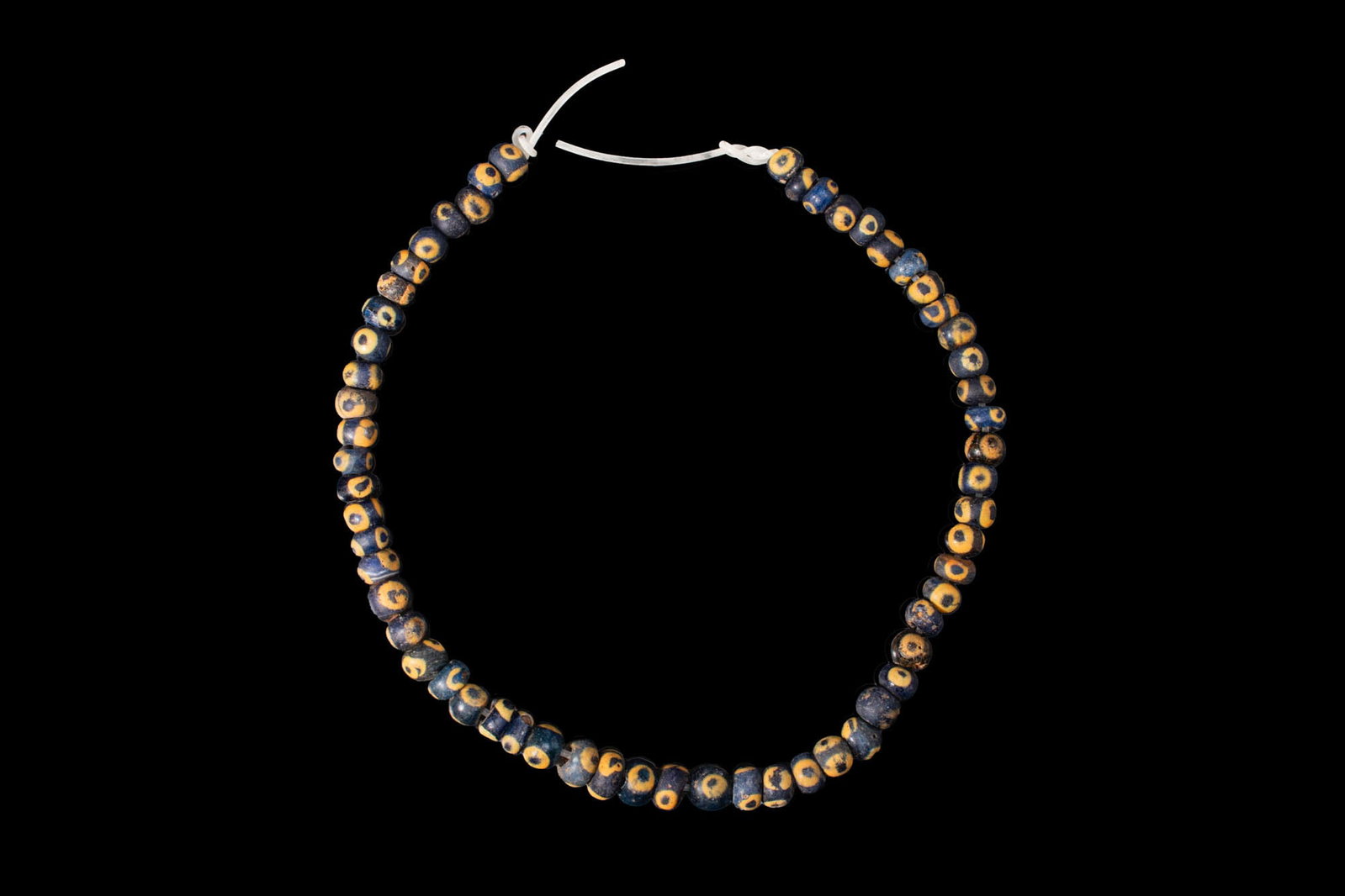 PHOENICIAN BLUE GLASS EYE BEAD NECKLACE: Ca. 600 - 300 BC. A necklace strand composed of blue glass beads of rounded form, each decorated with yellow and blue eye motifs. For similar see: Christie's, Live Auction, ancient glass formerly in t