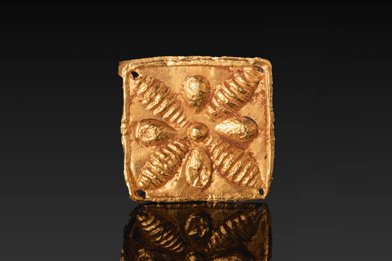 PHOENICIAN GOLD APPLIQUE WITH FLOWER MOTIF: Ca. 800 - 600 BC. A square-shaped gold applique with small perforations at each corner for attachment. The surface is decorated in repousse with a central boss surrounded by four teardrop-shaped petal