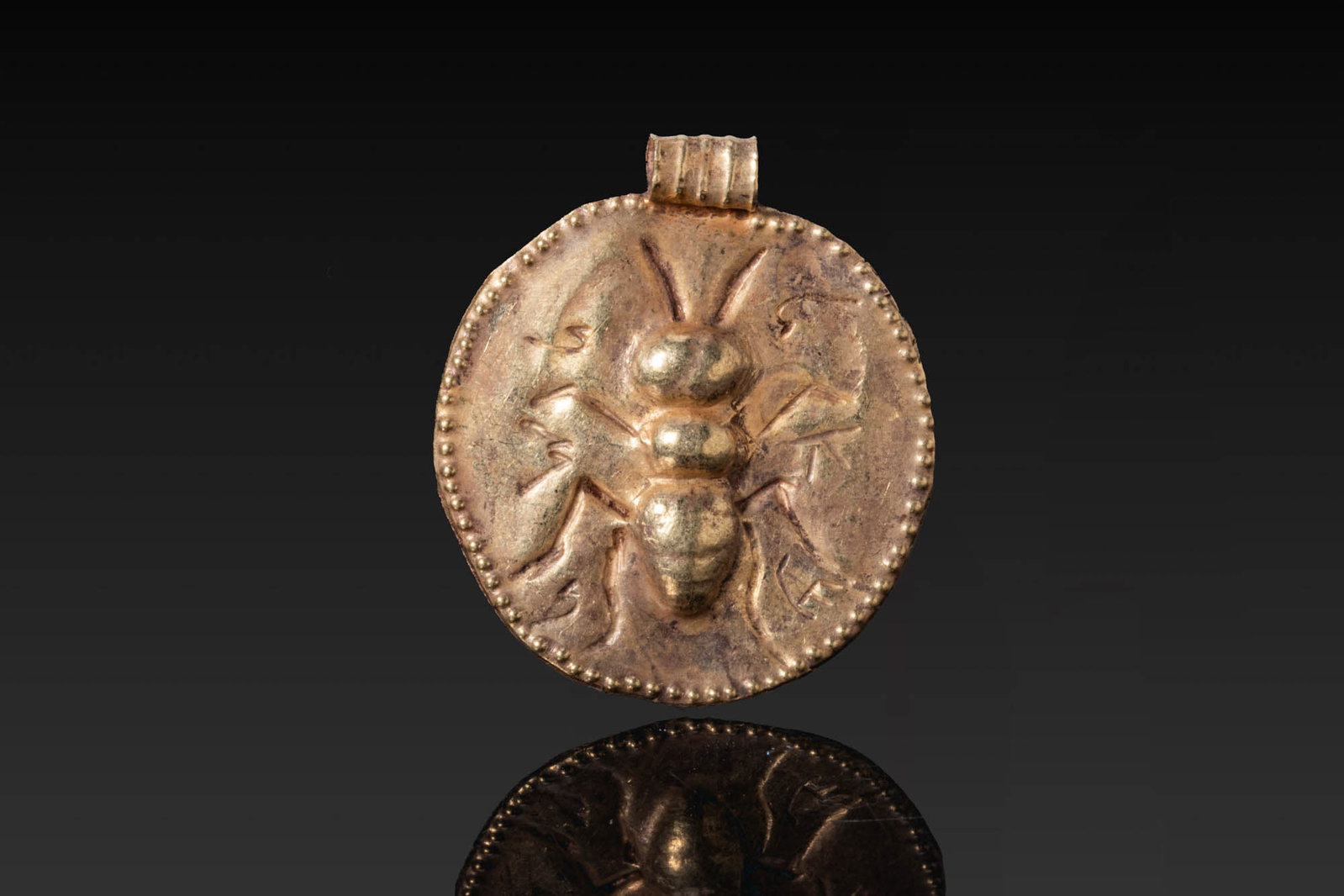 ROMANO-EGYPTIAN GOLD PENDANT WITH ANT: Ca. 30 BC - AD 200. A circular gold pendant with a repousse ant within a beaded border, with a suspension loop above. Size: 28mm x 24mm; Weight: 1.6g Provenance: London private collection; Munich acqu