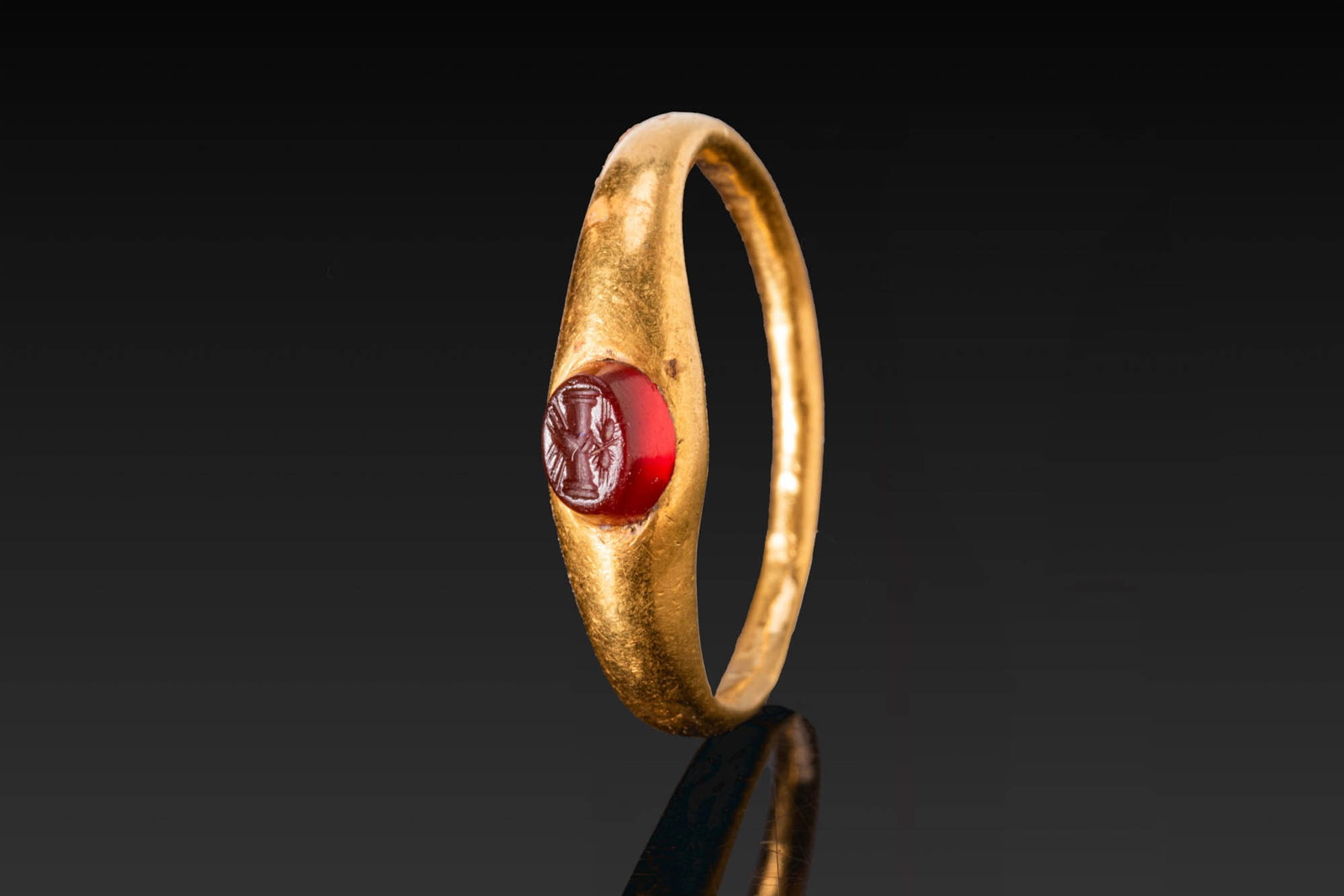 ROMAN GOLD RING WITH RED GARNET INTAGLIO OF CLASPED HANDS: Ca. AD 1 - 300. A gold ring with a slender tapering hoop and an oval bezel set with a red garnet intaglio engraved with clasped hands surmounted by two ears of wheat. For a similar symbol, see: The Br
