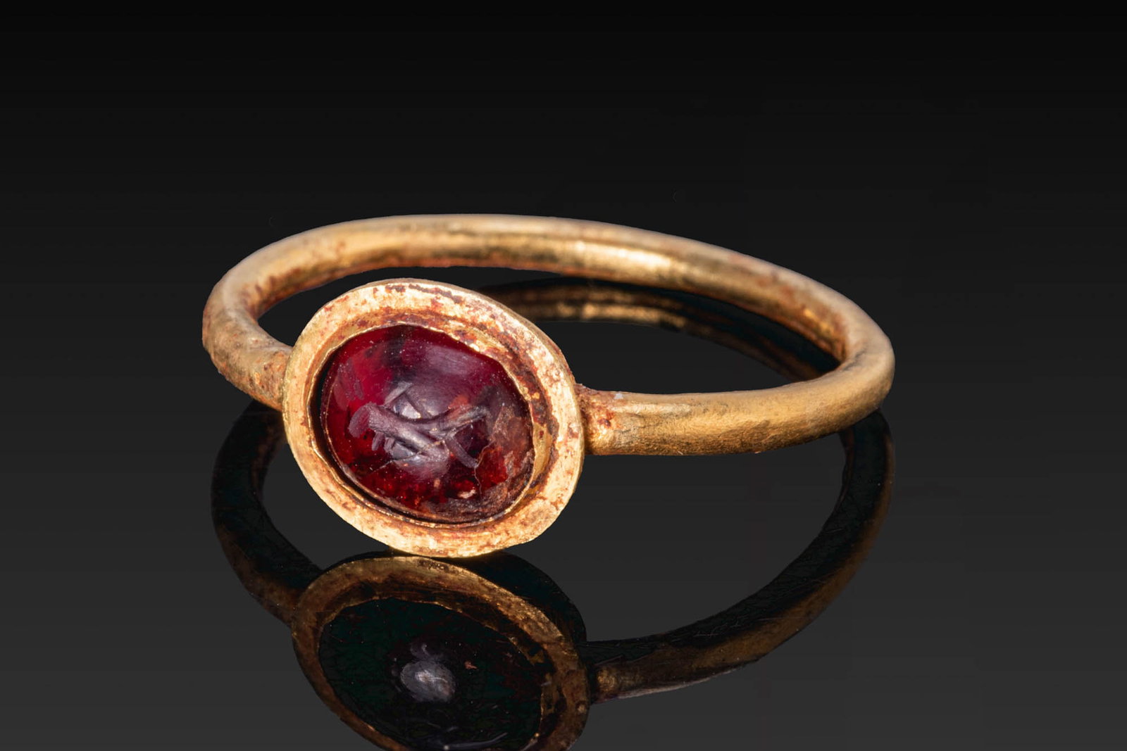 SASANIAN GOLD RING WITH RED GARNET INTAGLIO OF A BIRD: Ca. AD 600. A gold ring with a slender circular hoop and an oval bezel set with a red garnet intaglio engraved with a bird in profile. For similar see: C. J. Brunner, Sasanian Stamp Seals in The Metro