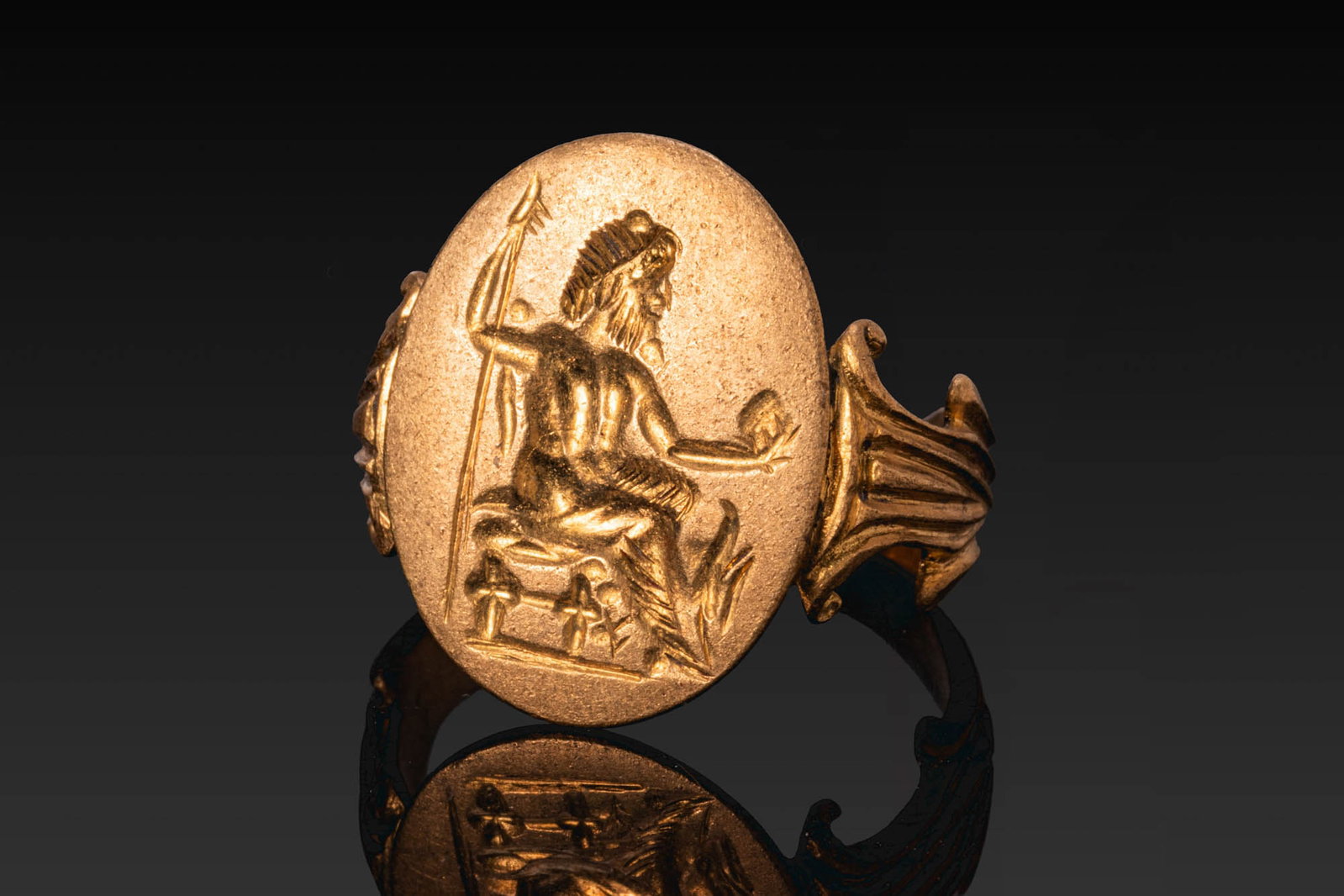 RARE ROMAN GOLD RING WITH JUPITER AND THE EAGLE: Ca. AD 300 (or later). A gold ring with a flat-section hoop and fluted shoulders with volutes, leading to a broad oval bezel engraved with Jupiter seated on a throne in profile, holding a long sceptre