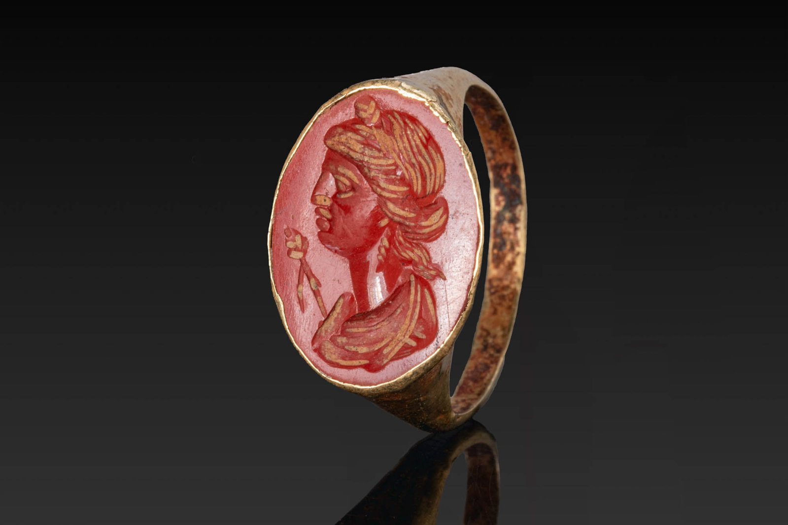 ROMAN GOLD RING WITH RED JASPER INTAGLIO OF CERES: Ca. 100 BC - AD 100. A gold ring with a tapering hoop and an oval bezel set with a red jasper intaglio engraved with the profile bust of Ceres, her hair bound in a chignon, with drapery at the shoulde