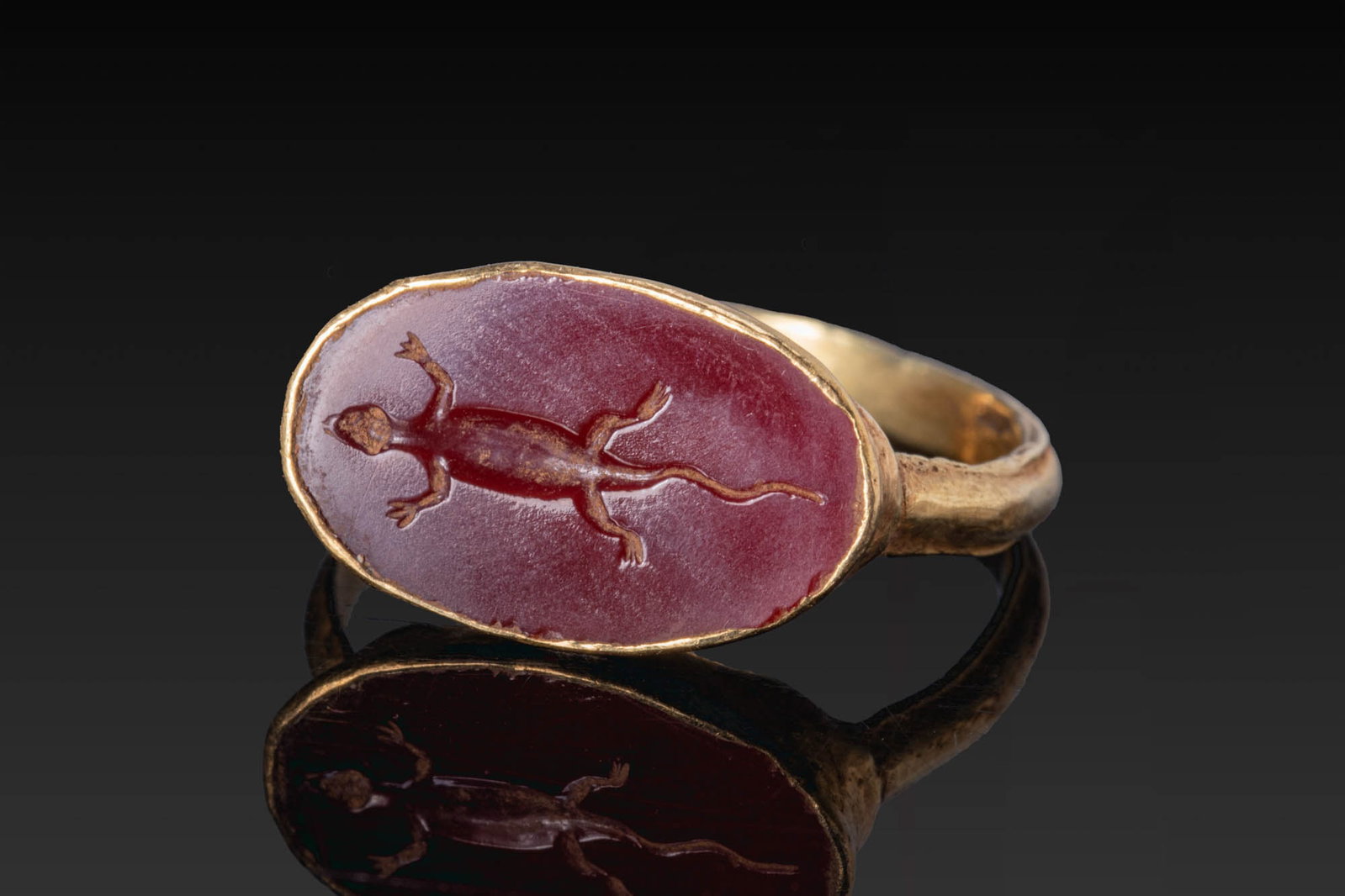 ROMAN RED GARNET INTAGLIO OF A LIZARD IN GOLD RING: Ca. AD 200 - 400. A garnet intaglio engraved with a lizard seen from above, mounted in a possibly later gold ring with a slender hoop and an oval bezel. For similar see: The British Museum, Museum num