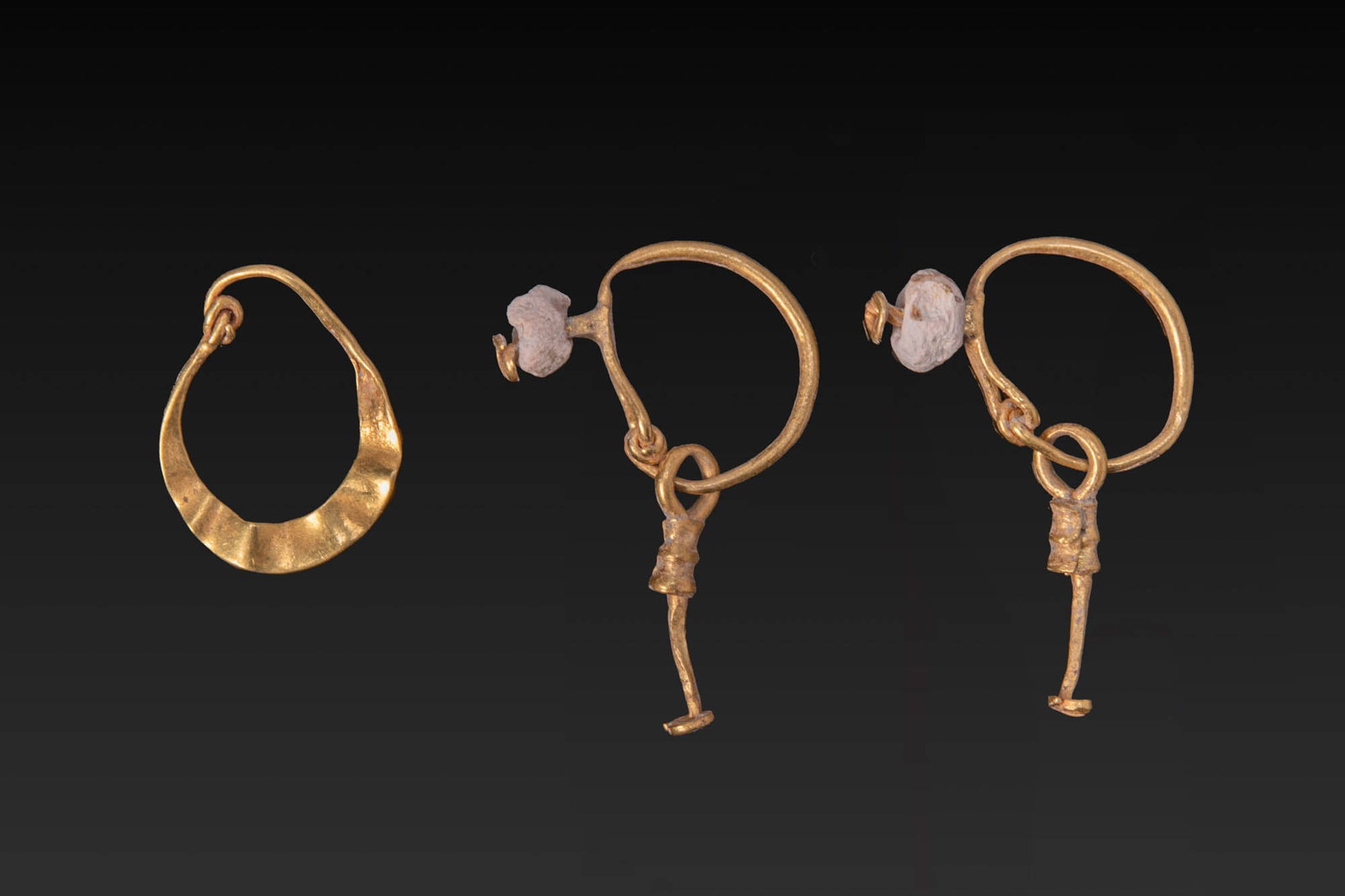 COLLECTION OF ROMAN GOLD EARRINGS: Ca. AD 1 - 300. A collection of three gold earrings, including, from left to right: a flat hoop of tapering profile with overlapping terminals; and a matched pair of gold earrings, each formed as a ci