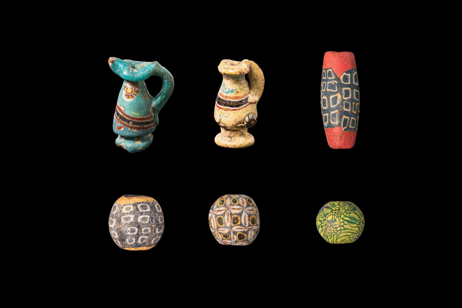 COLLECTION OF GRAECO-ROMAN GLASS JUGLET PENDANTS AND BEADS: Ca. 200 - 1 BC. A collection of six glass ornaments, including, from left to right: a pair of turquoise and yellow glass juglet pendants, each with a piriform body, a trefoil mouth, a loop handle join