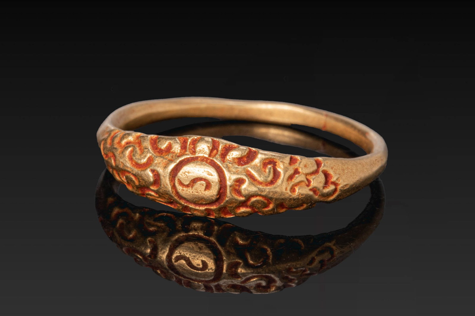 MEDIEVAL JAVANESE GOLD RING: Ca. AD 700 - 1000. A gold ring with a slender hoop widening to an elongated bezel decorated with scrolling ornament centred by a circular motif. Size: D:16.1mm / US: 5 1/2 / UK: K 1/2; Weight: 2.5g Pr