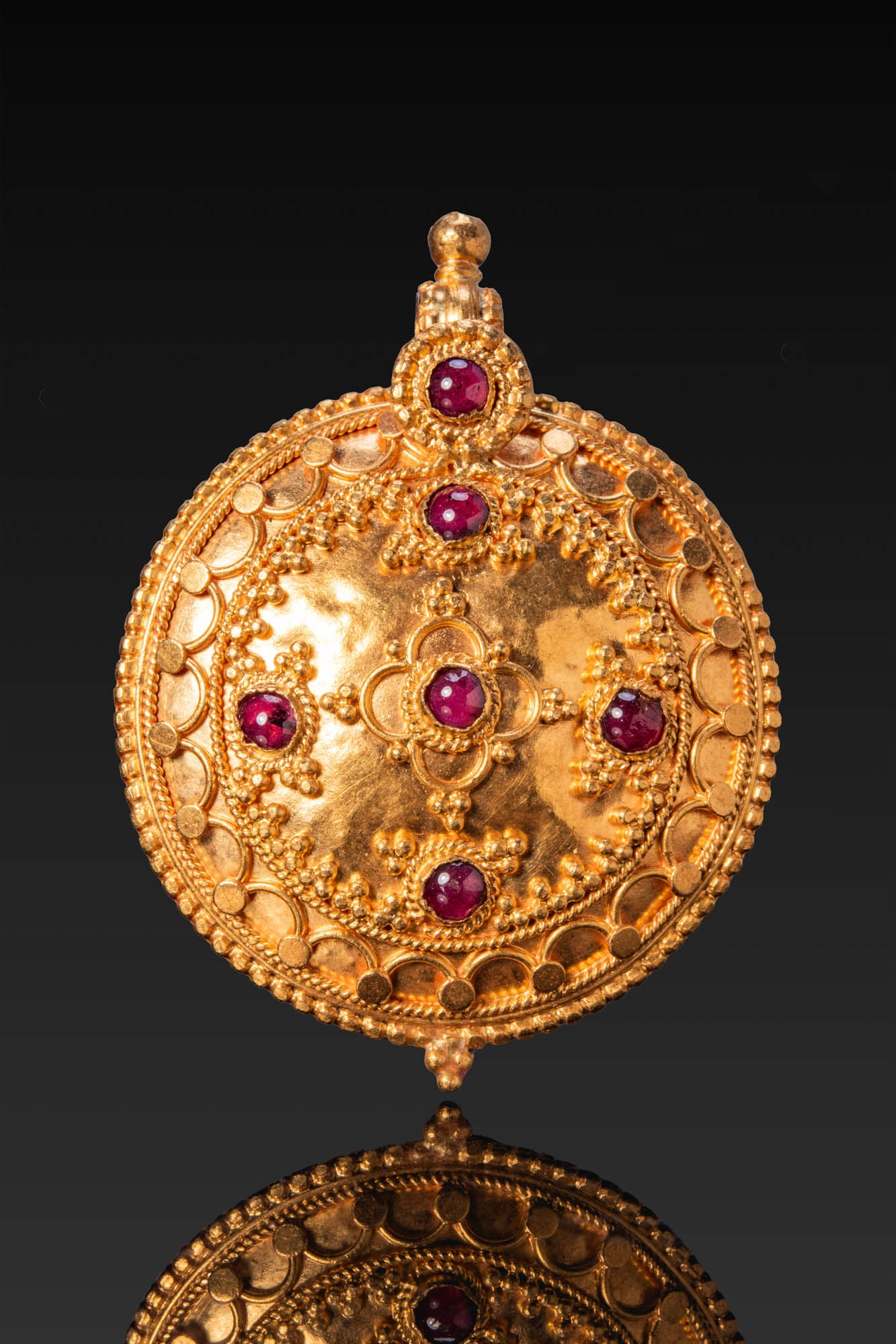 BYZANTINE LARGE GOLD AND GARNET MEDALLION: Ca. AD 700 - 1200 (or later). A gold medallion of domed profile with a beaded outer border and a band of repeating roundels and arches enclosed by twisted wire bands. The centre is set with five garne