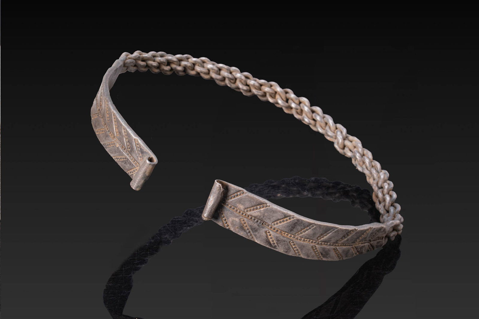 VIKING SILVER BRAIDED BRACELET WITH STAMPED FINIALS: Ca. AD 800 - 1000. A silver penannular bracelet with a braided shank widening at each end into flat flaring finials with rolled edges, decorated with a central row of stamped dots with short diagonal 