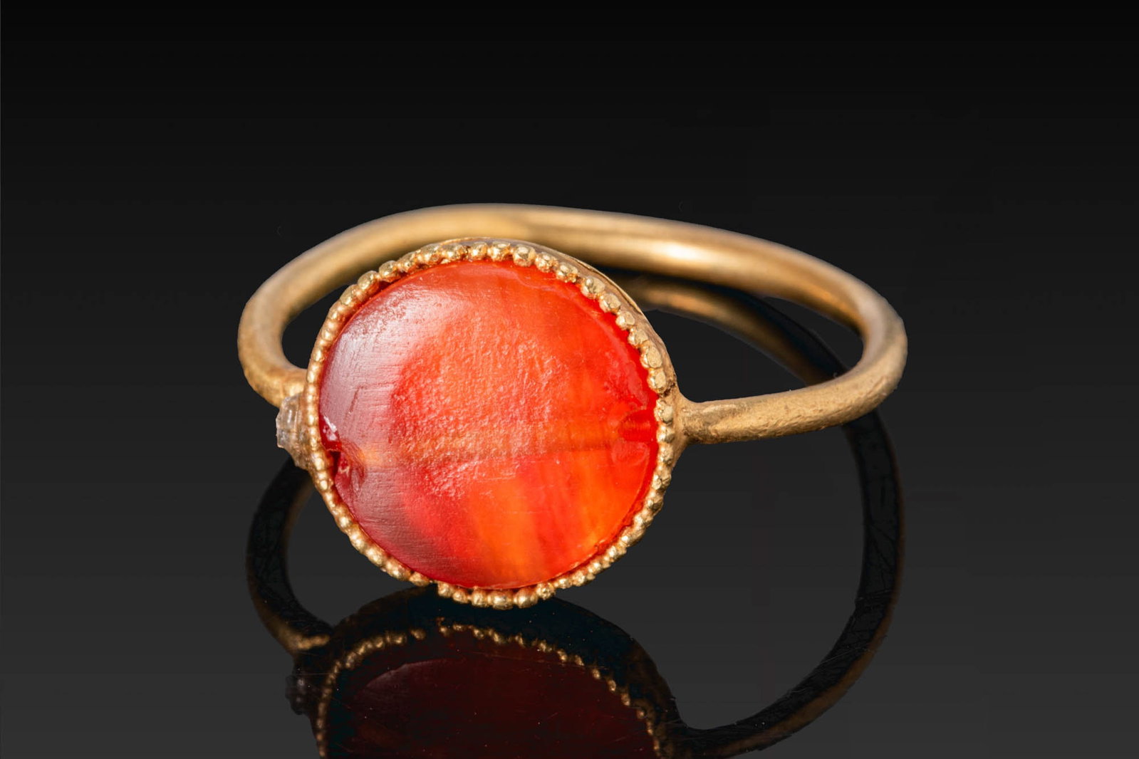 BYZANTINE GOLD RING WITH CARNELIAN CABOCHON: Ca. AD 600. A gold ring with a slender circular hoop and an oval bezel set with a carnelian cabochon within a beaded border. Size: D:15.49mm / US: 4 3/4 / UK: J; Weight: 1.8g Provenance: Private Londo