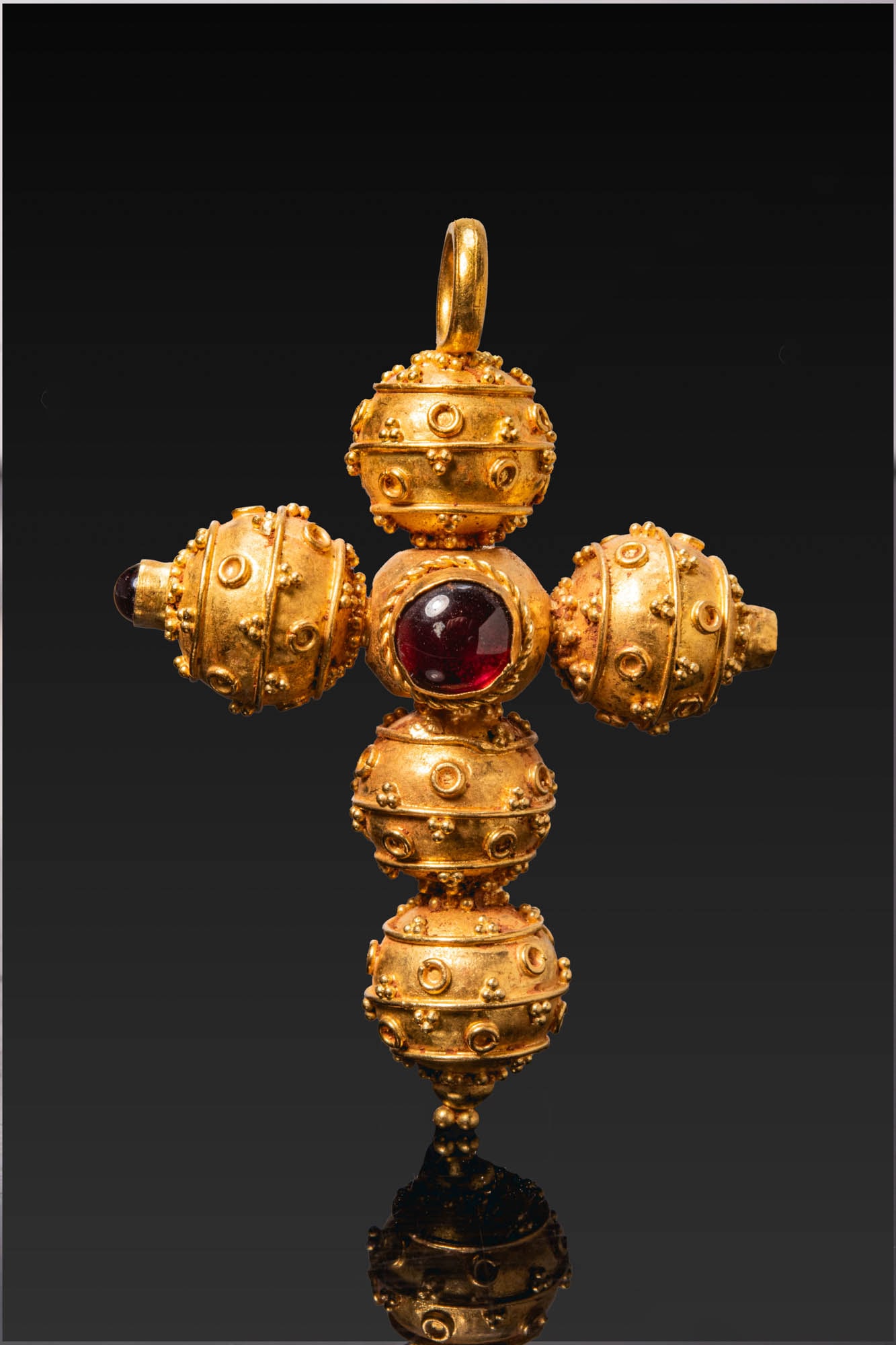 LATE BYZANTINE GOLD CROSS WITH FILIGREE AND GARNET CABOCHONS: Ca. AD 1200 - 1400 (or later). A gold cross pendant composed of hollow spheres arranged around a central round garnet cabochon in a mount with a twisted wire border, with one sphere on each arm and tw