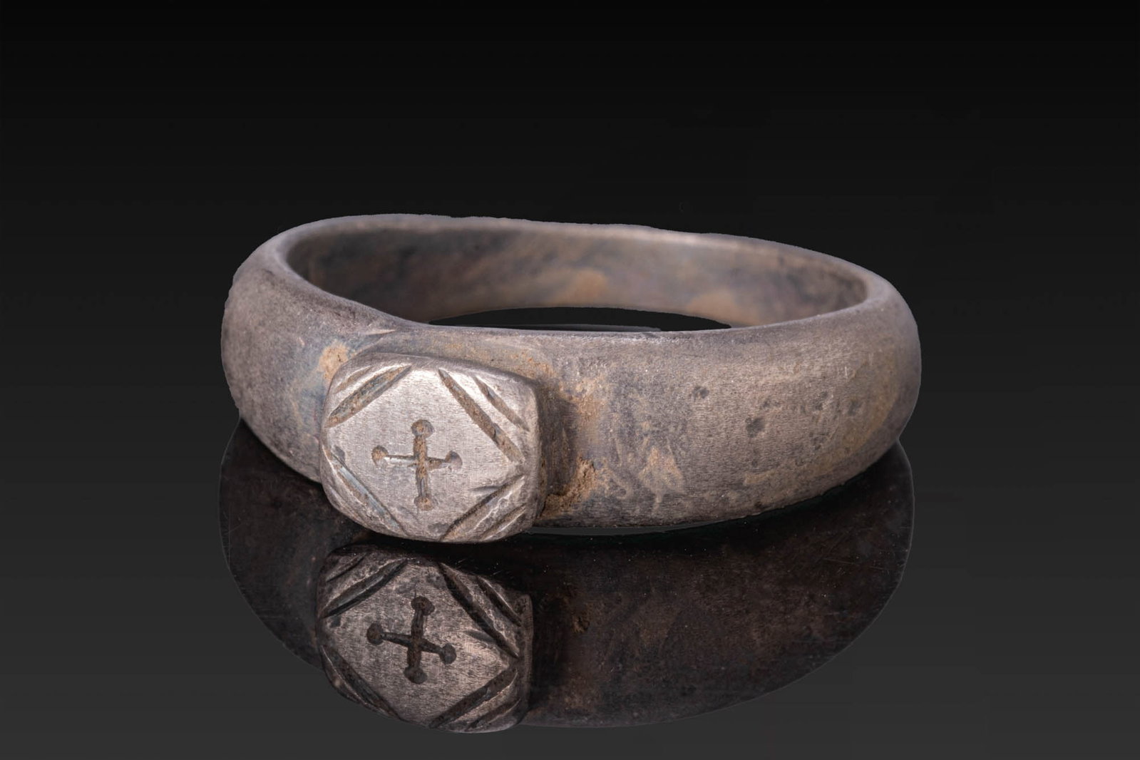 BYZANTINE SILVER RING WITH A CROSS: Ca. AD 300 - 500. A silver ring with a broad rounded hoop and a rectangular bezel with chamfered corners, engraved with a cross with rounded finials. Size: D:18.54mm / US: 8 1/2 / UK: Q 1/2; Weight: 6