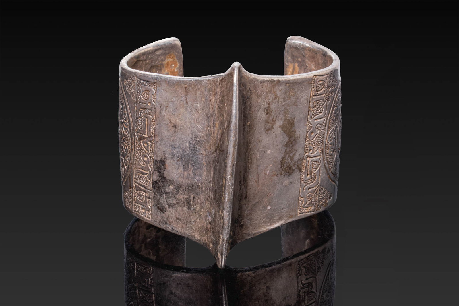 SELJUK SILVER BRACELET: Ca. AD 1000 - 1100. A silver bracelet of broad open form with a pronounced central ridge and slightly flaring terminals, each engraved with a rosette enclosed by a border of stylised birds. Beside eac