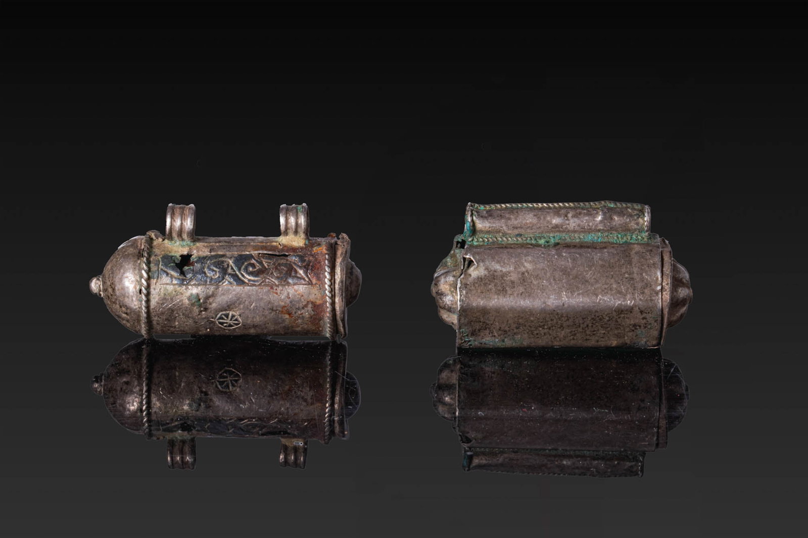 PAIR OF SELJUK SILVER AND NIELLO SCROLL PENDANTS: Ca. AD 1000 - 1200. A pair of silver scroll pendants, from left to right: a cylindrical pendant with domed terminals, two ribbed loops above, and niello interlace panels; and a pendant formed as a tub