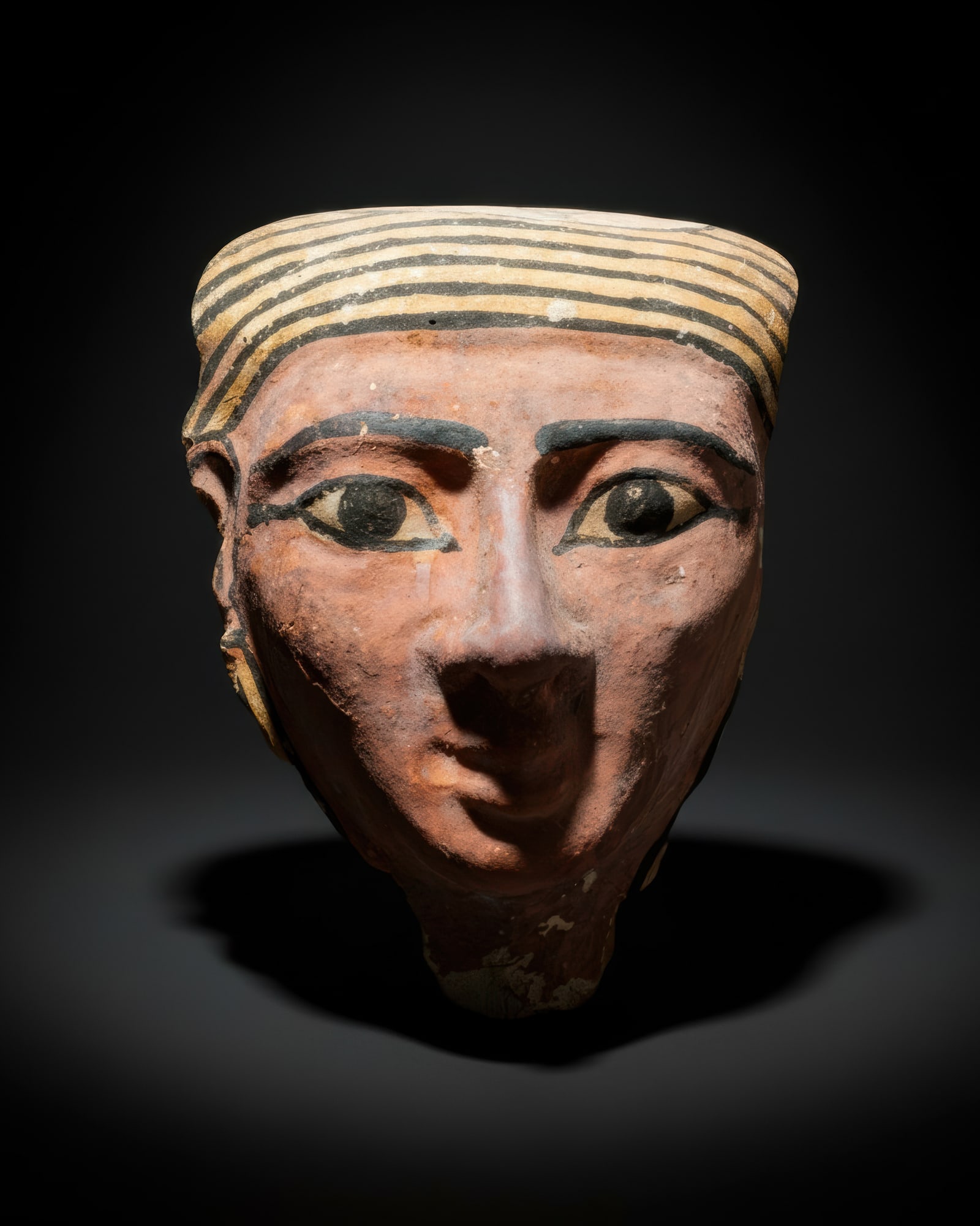 HUGE EGYPTIAN COFFIN MASK: Late Period, Ca. 664 - 332 BC. A coffin mask with a layer of plaster overlay and painted surface. The face is broad and tapering, painted in a reddish pink, with large almond-shaped eyes outlined in b