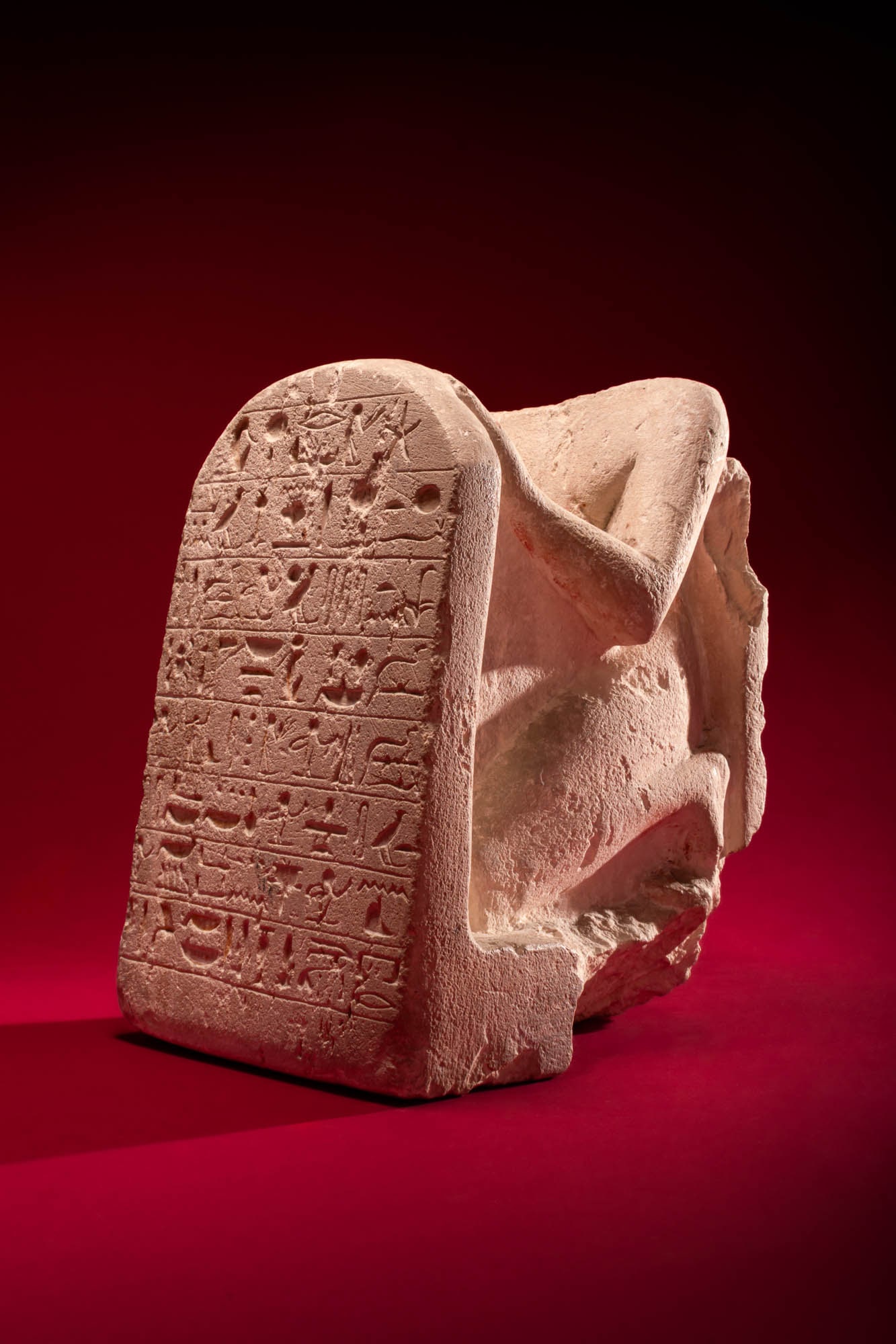 STUNNING EGYPTIAN LIMESTONE STELOPHOROUS STATUE WITH INSCRIBED STELA: New Kingdom, Ca. 1294 - 1250 BC. A limestone stelophorous statue of a kneeling man on an integral base, wearing a long skirt and supporting a tall rounded stela in front of him. The surface of the ste