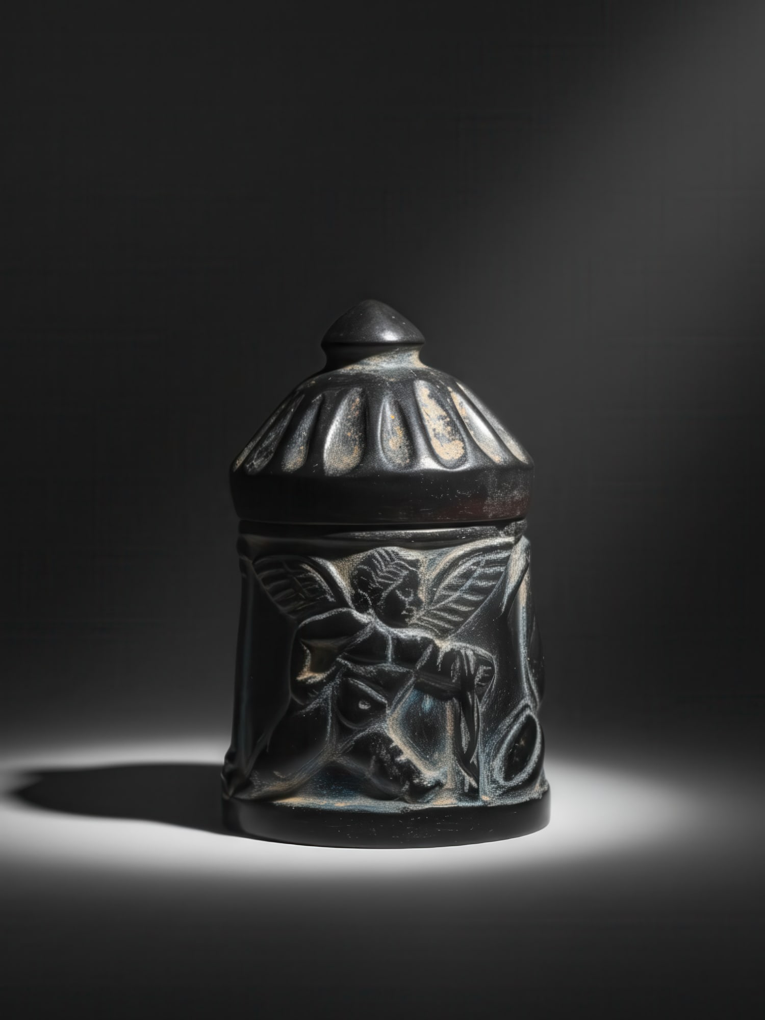 ROMAN OR BYZANTINE STONE PYXIS WITH PUTTI: Ca. AD 400 - 600. A stone pyxis with a cylindrical body spreading slightly towards the flat base, and a domed fluted lid surmounted by a conical knop. The sides are carved in low relief with two playf