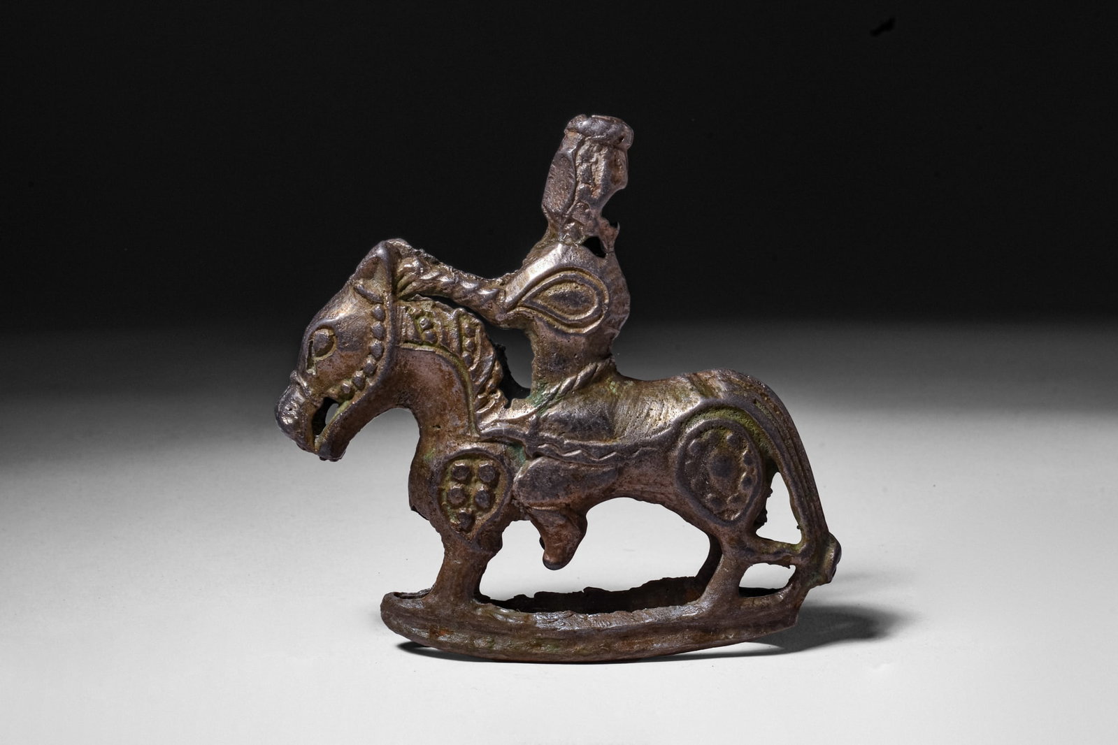RARE VIKING SILVER ALLOY POMMEL WITH HORSEMAN: Ca. AD 900 - 1000. A silver alloy pommel cast as an armoured man seated on a horse above a curved base. The rider wears a tall cylindrical helmet and armour, and extends both hands towards the horse's