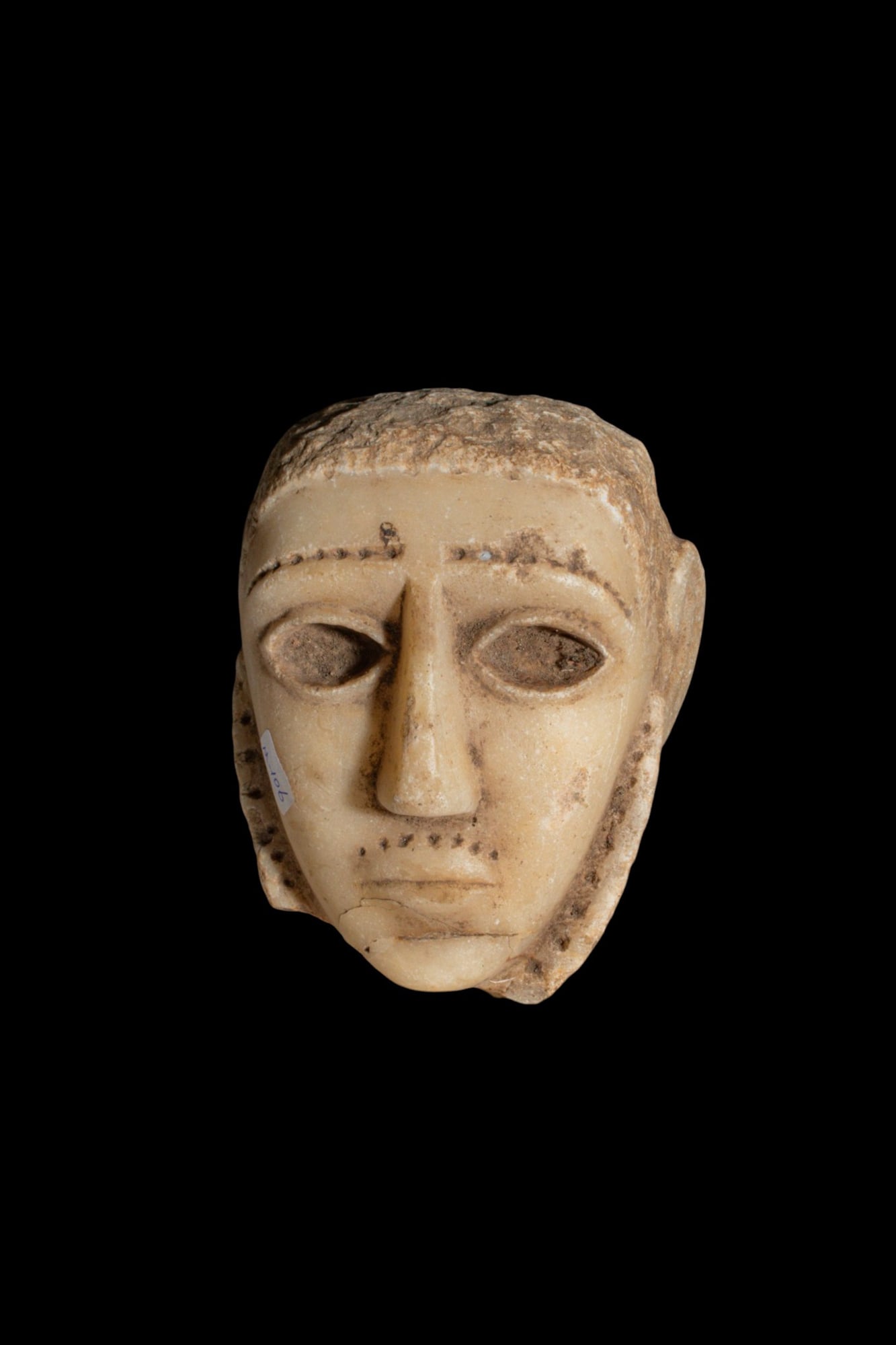 SOUTH ARABIAN ALABASTER HEAD OF A MAN: Ca. 300 - 100 BC. An alabaster head of a man with a broad face, short hair, and large almond-shaped eyes recessed for inlays. The arched brows, moustache, and short beard are marked by rows of drilled