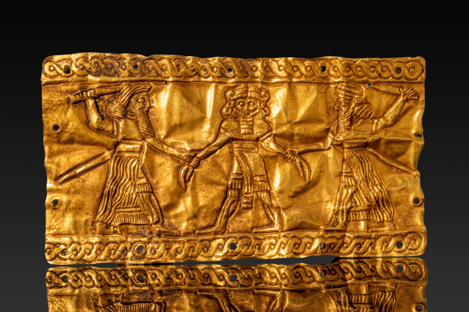 MESOPOTAMIAN GOLD LEAF WITH A DEITY AND TWO HEROES: Ca. 2200 - 1800 BC. A rectangular gold leaf in repousse with three standing figures in a single register between rope-twist borders. At the centre stands a deity wearing a horned headdress. On either 