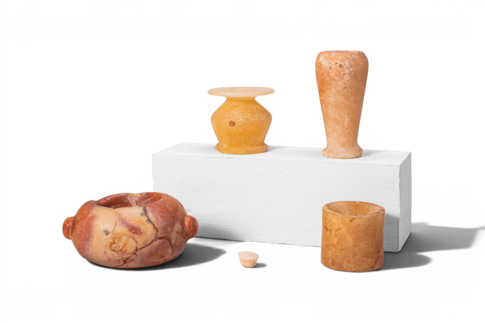 COLLECTION OF EGYPTIAN STONE VESSELS: Ca. 2600 - 1069 BC. A collection of four stone vessels, including, from left to right: a squat vessel with a carinated body, short neck, broad flaring rim, and a matching stopper; a tall, inverted pir