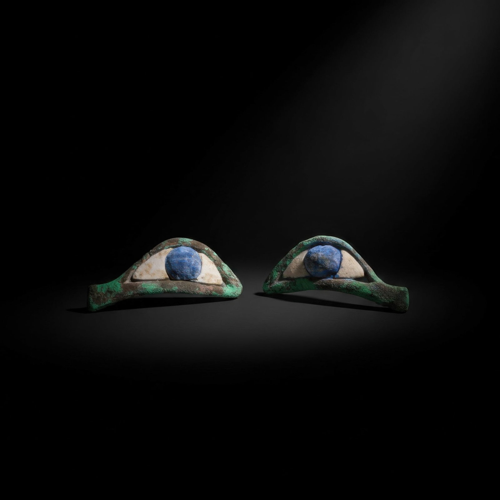PAIR OF EGYPTIAN BRONZE AND STONE EYES: Late Period, Ca. 664 - 332 BC. A pair of eye inlays formed as elongated bronze frames with pointed inner and outer corners, each set with a white stone sclera and a blue stone iris. For similar see: M