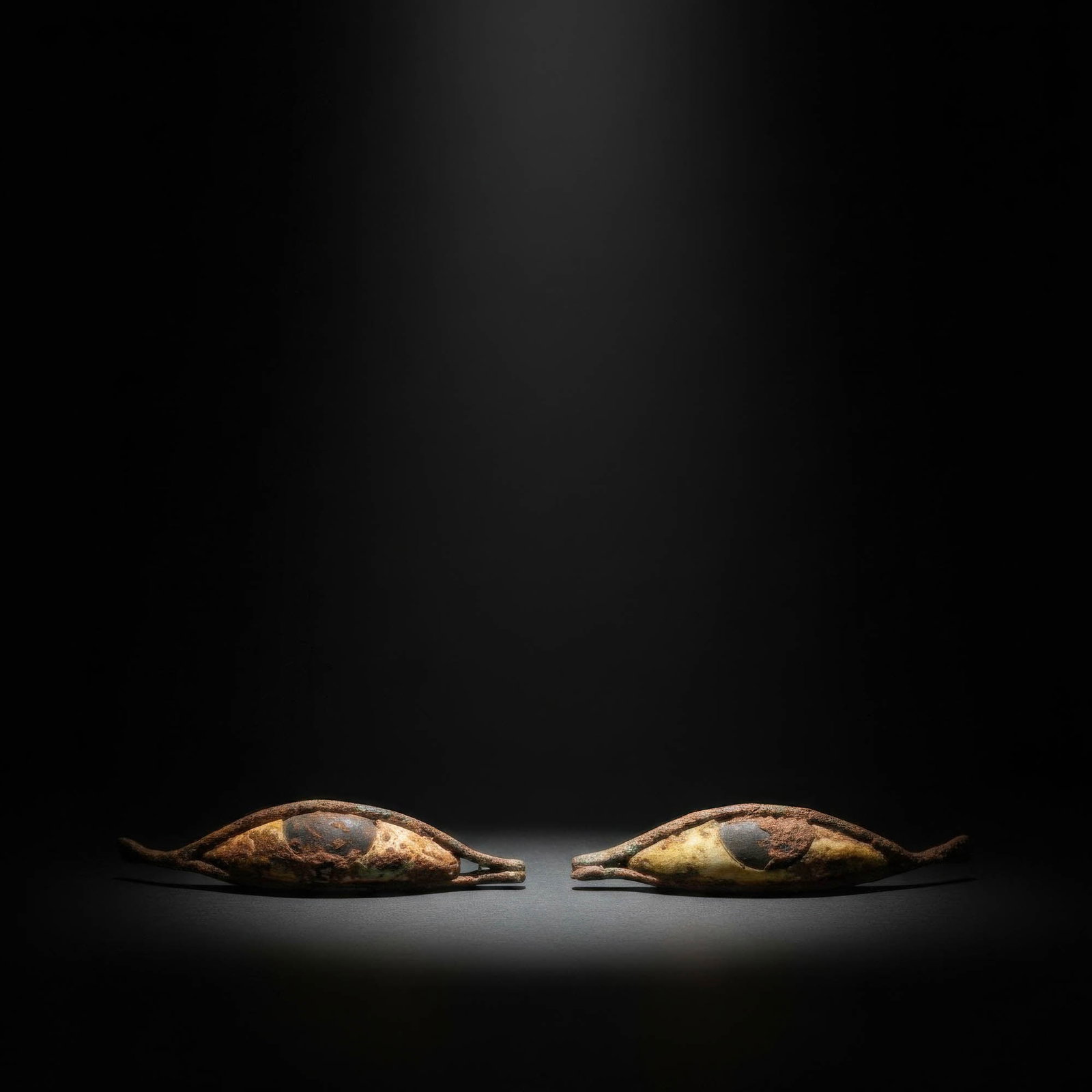 PAIR OF EGYPTIAN BRONZE AND STONE EYES: Late Period, Ca. 664 - 332 BC. A pair of eye inlays formed as elongated bronze frames with pointed inner and outer corners, each set with a white stone sclera and a black stone iris. For similar see: 