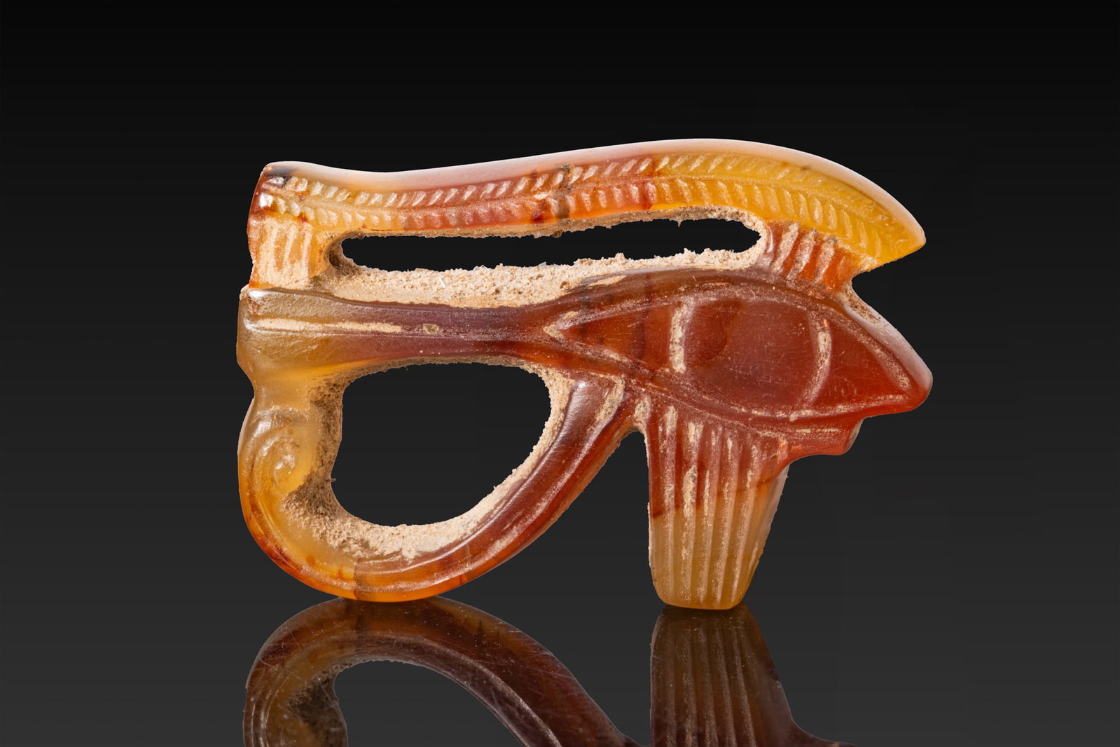 RARE EGYPTIAN CARNELIAN WEDJAT EYE AMULET: Late Period, Ca. 664 - 332 BC. An openwork carnelian wedjat eye amulet with an almond-shaped eye, a long tapering cosmetic line, and a curved cheek marking below. The eyebrow is marked with a chevron 