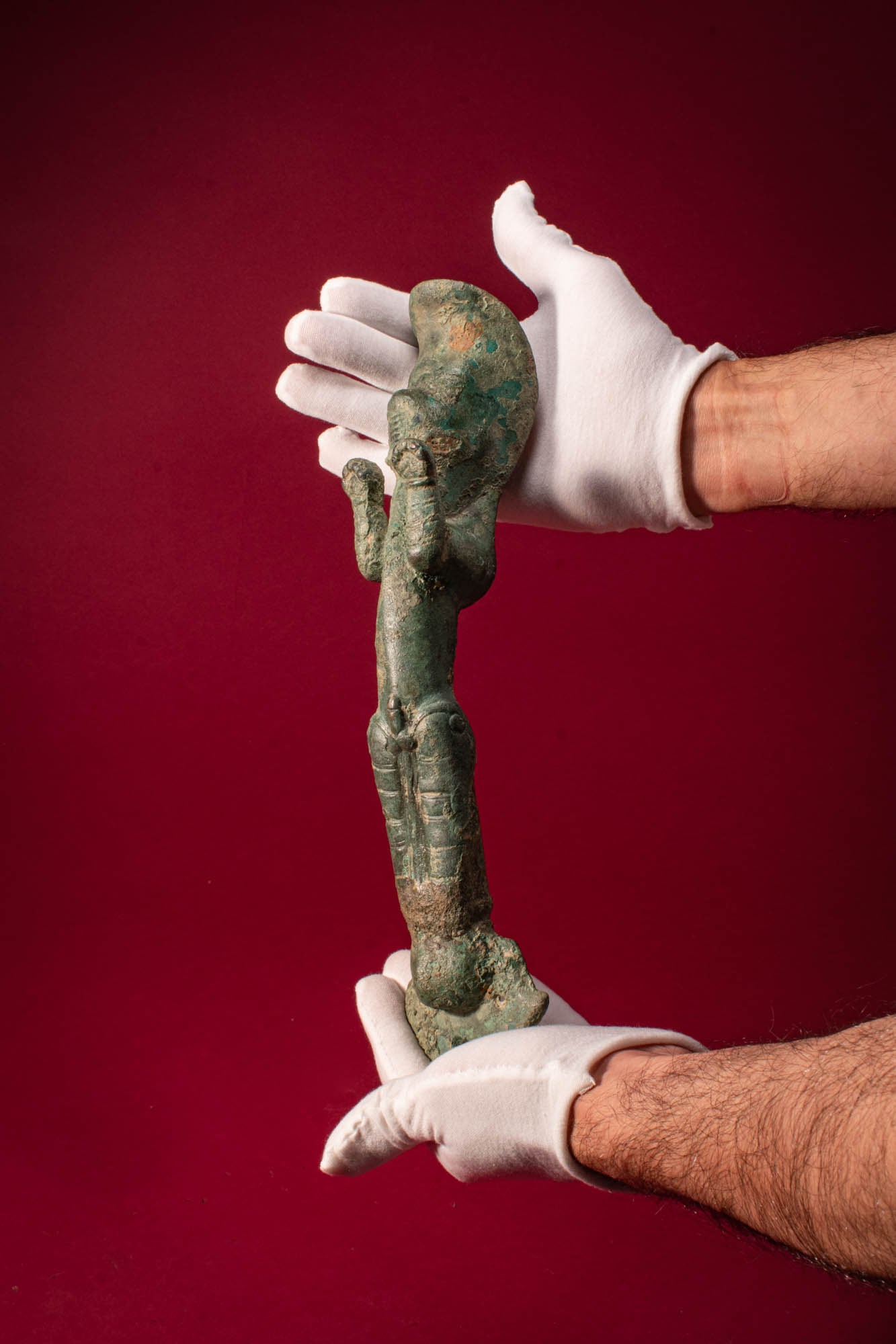 LARGE GREEK PERIOD BRONZE ZOOMORPHIC HANDLE FROM VESSEL: Ca. 500 BC. A cast bronze zoomorphic handle in the shape of a stylised animal forming an elongated shaft. The head is rendered with a projecting muzzle flanked by raised forelegs, the lower section wi