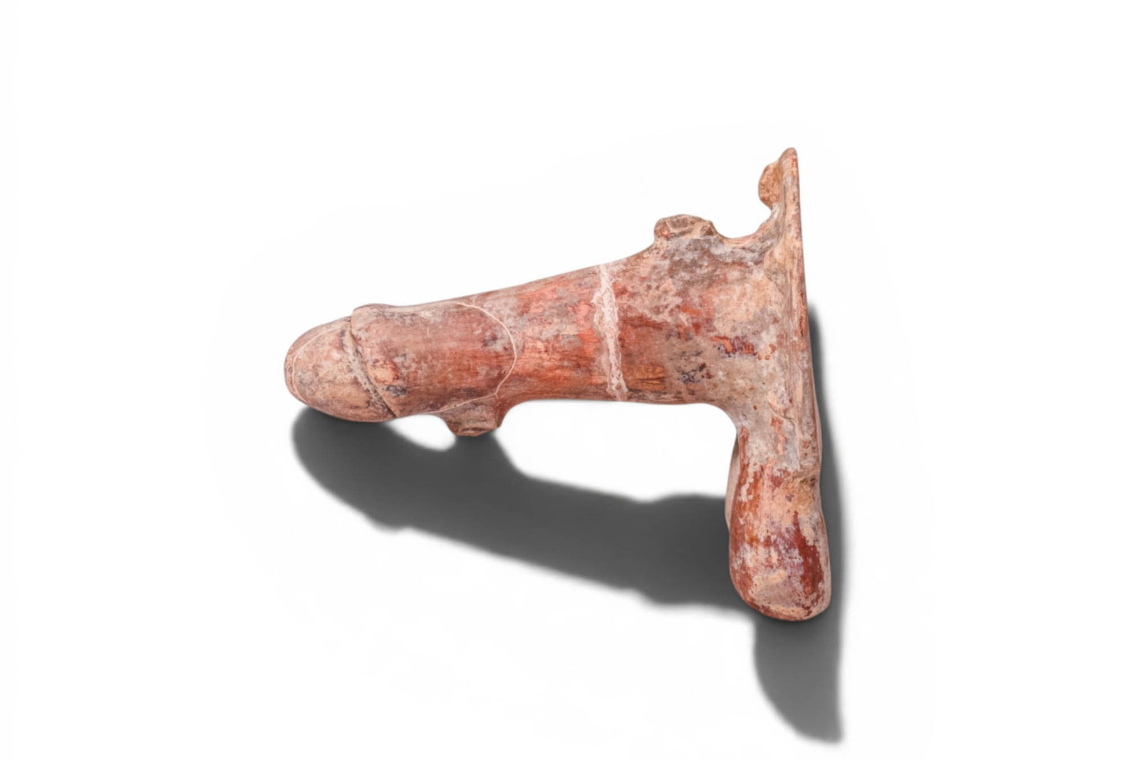 ETRUSCAN (or later) PHALLIC AMULET WITH APOTROPAIC MASKS: Ca. 300 BC. A hollow terracotta phallic amulet with a cylindrical shaft, rounded glans, and paired testicles. The broad circular base is set with raised apotropaic masks around the rim, each rendered 