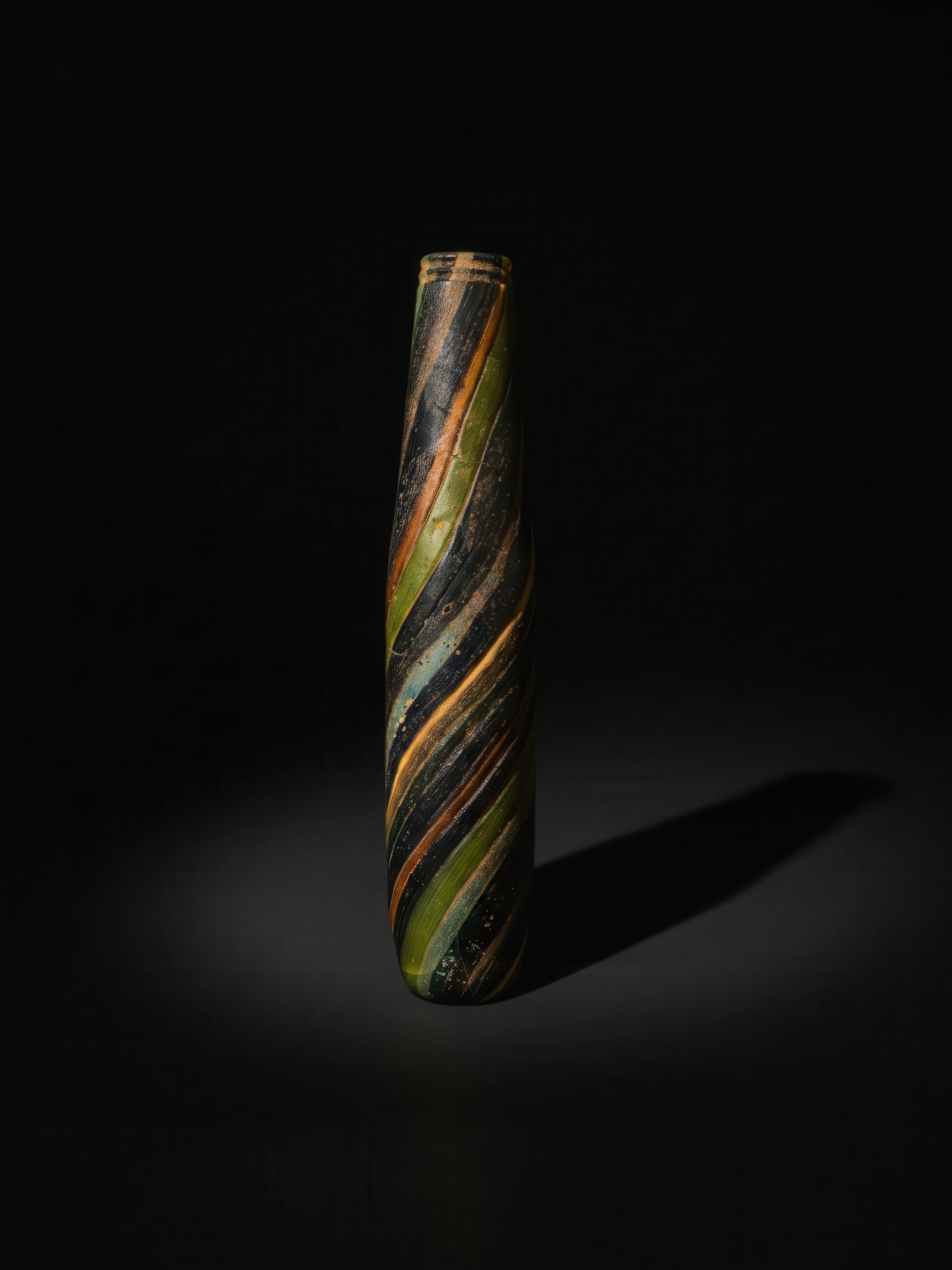 ROMAN POLYCHROME BANDED GLASS ALABASTRON: Ca. 100 BC - AD 100. A polychrome glass alabastron with a flat rim, a collared neck, and a long cylindrical body broadening slightly towards the rounded base. The vessel is formed from spiralling band