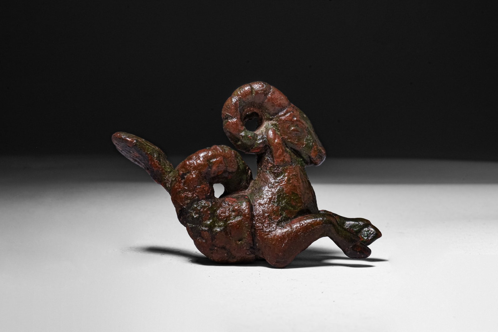 LARGE ROMAN BRONZE FIGURINE OF A CAPRICORN: Ca. AD 1 - 200. A bronze figurine of a capricorn, with the forepart of a goat and an upturned fish tail. The head has a tapering muzzle and tightly curled horns, and the forelegs are folded beneath th