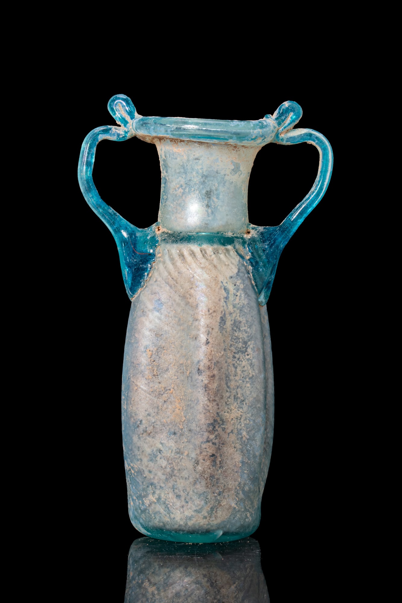 SUPERB LATE ROMAN BLUE GLASS AMPHORISKOS: Ca. AD 300 - 500. A translucent pale blue amphoriskos with a cylindrical body with concave sides, decorated with spiral ribs, below a short neck and a folded rim. Two applied handles in darker blue gl