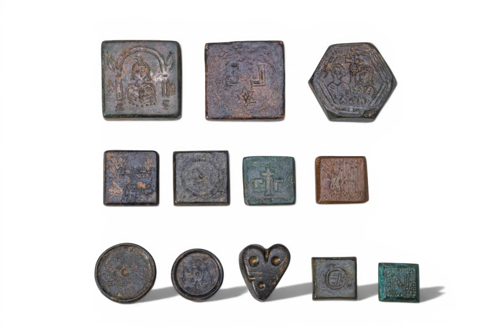 COLLECTION OF BYZANTINE BRONZE INLAID WEIGHTS: Ca. AD 600 - 900. A collection of 12 bronze inlaid weights, including square, circular, hexagonal and heart-shaped examples, each engraved with denominational marks, incised decoration and weight symb