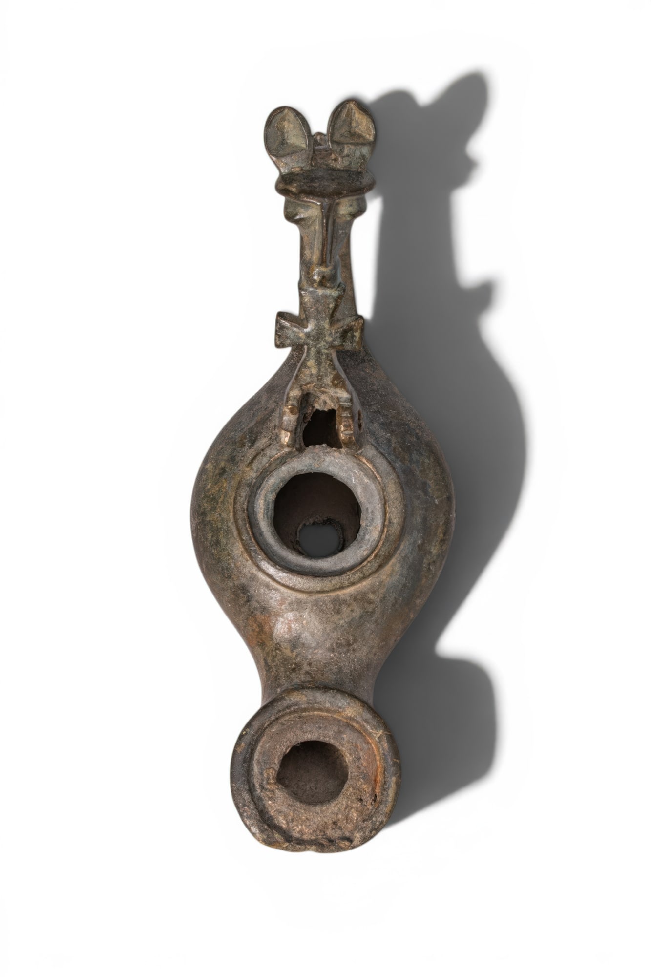 BYZANTINE BRONZE OIL LAMP WITH HORSE-SHAPED HANDLE AND CROSS: Ca. AD 500 - 600. A bronze oil lamp with a rounded body tapering to a short nozzle and a broad filling hole at the centre. The handle is formed as an open loop surmounted by a stylised horse head, set