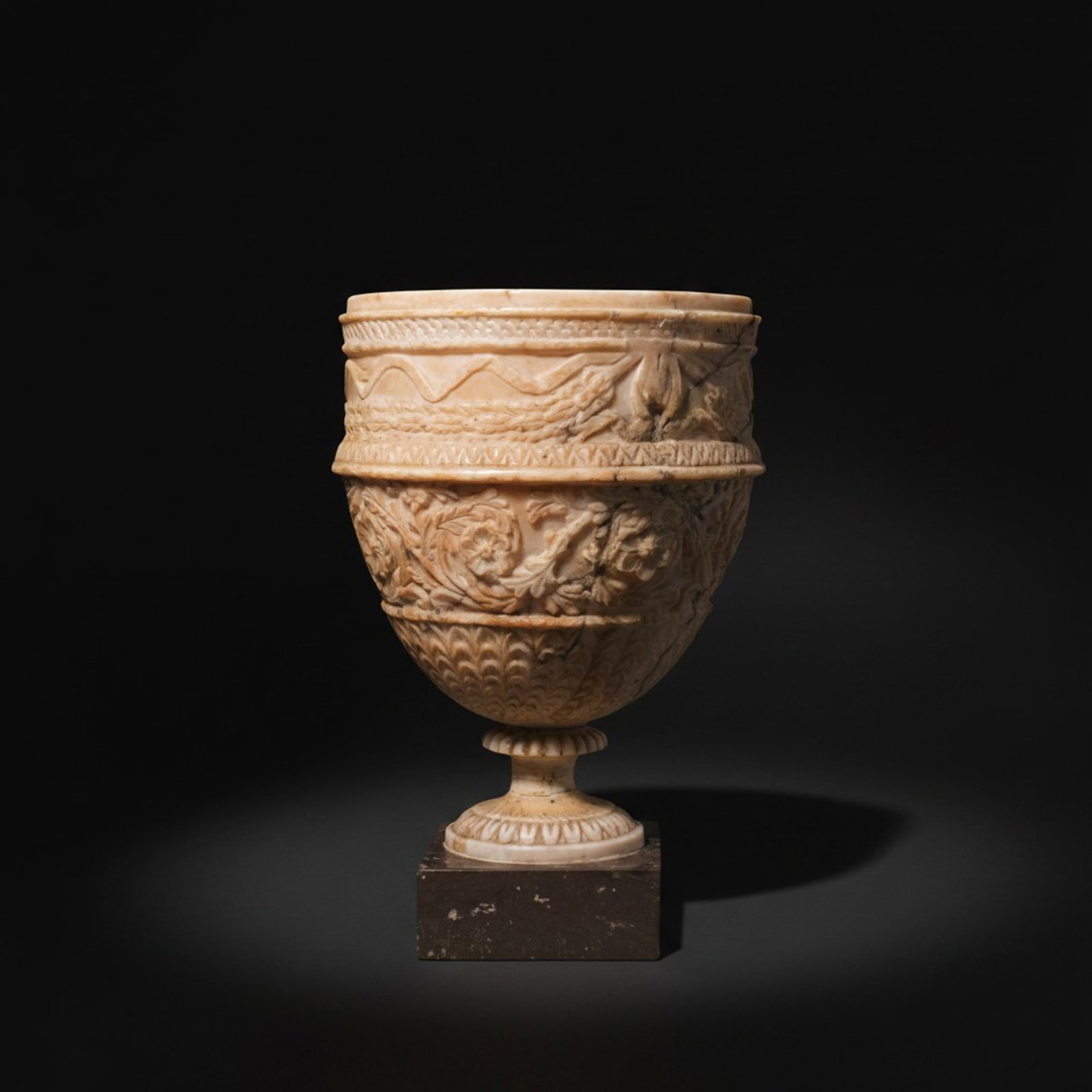 RENAISSANCE MARBLE CHALICE WITH RELIEF DECORATION: Ca. AD 1500 - 1700. A light marble chalice with a deep cup on a spreading foot, mounted on a stone base. The foot is carved with an egg-and-dart band, a striped moulding, and a ribbed upper section. T