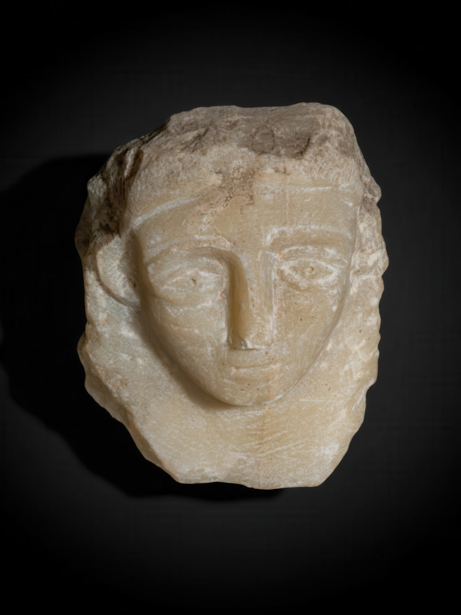 SOUTH ARABIAN ALABASTER HEAD: Ca. 300 - 100 BC. An alabaster head carved with a broad oval face, arched brows and large almond-shaped eyes with drilled pupils. The nose is long and straight, above a small mouth. The cheeks are ful