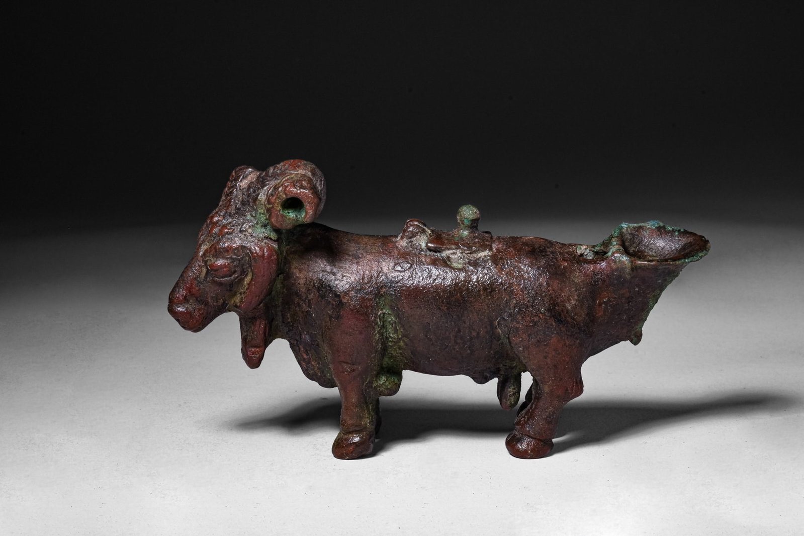 ROMANO-EGYPTIAN BRONZE RAM-SHAPED OIL LAMP: Ca. 100 BC - AD 100. A bronze oil lamp in the form of a ram standing on four short legs, the elongated body forming the reservoir, with the nozzle at the rear and a central filling hole on the back fi