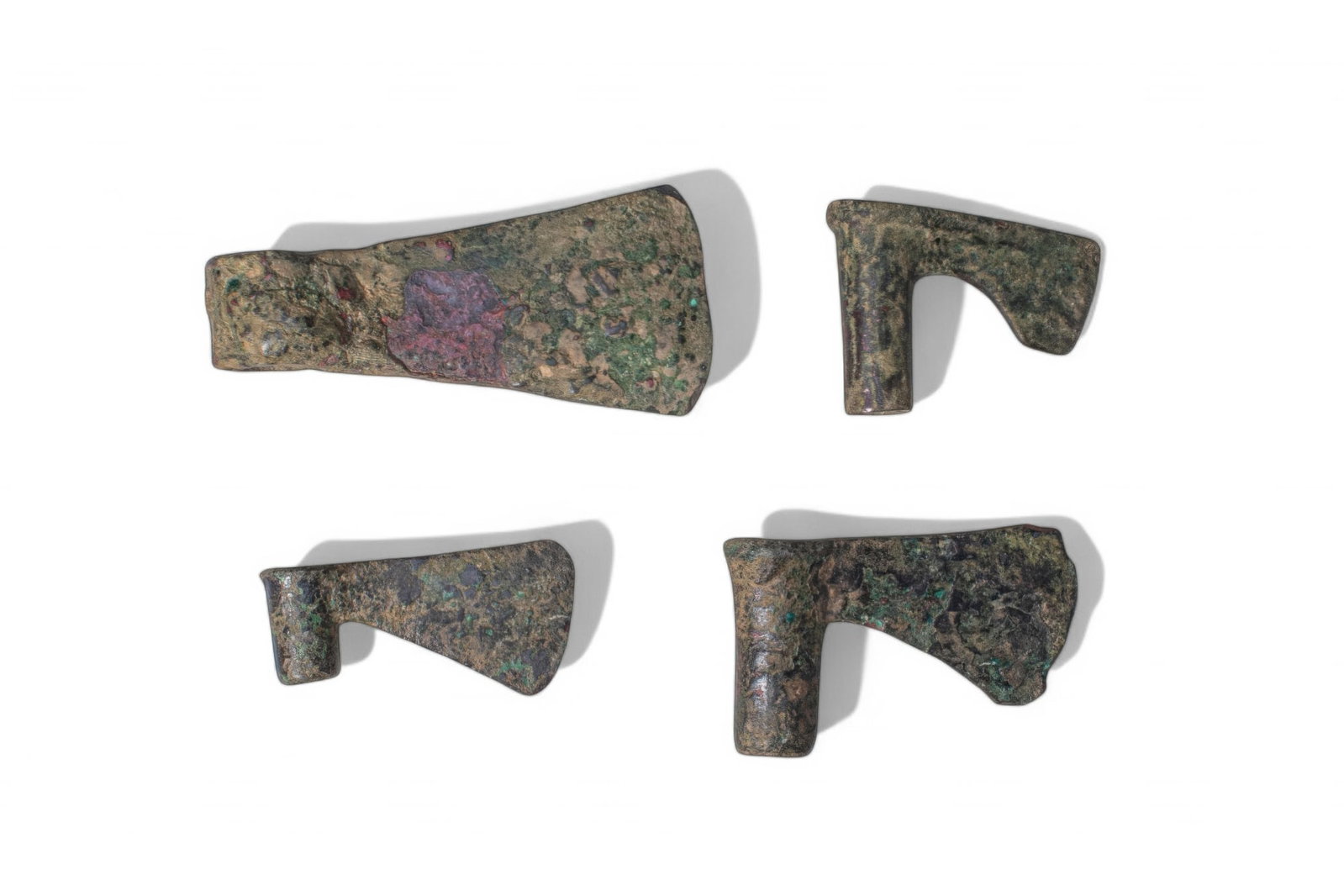 COLLECTION OF GREEK PERIOD BRONZE AXE HEADS: Ca. 1200 - 800 BC. A collection of four bronze axe heads, including, from top left: an axe head with a broad blade and a short cylindrical socket; and three examples of similar form, each with a short