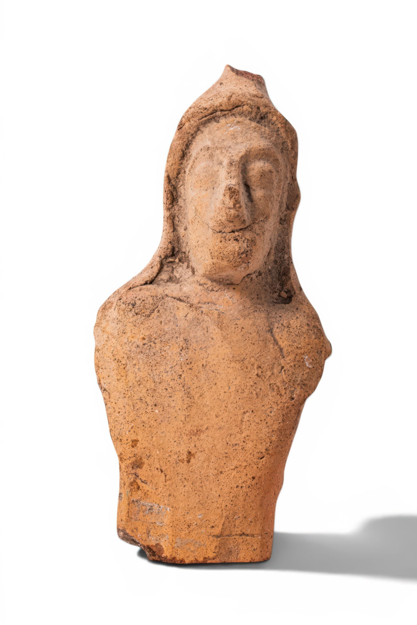 CYPRIOT TERRACOTTA MALE VOTIVE TORSO: Ca. 600 - 500 BC. A terracotta male votive torso with a flat tapering body and broad shoulders. The face is oval, with large eyes, a broad nose, and a projecting chin. The head is topped with a cap fa